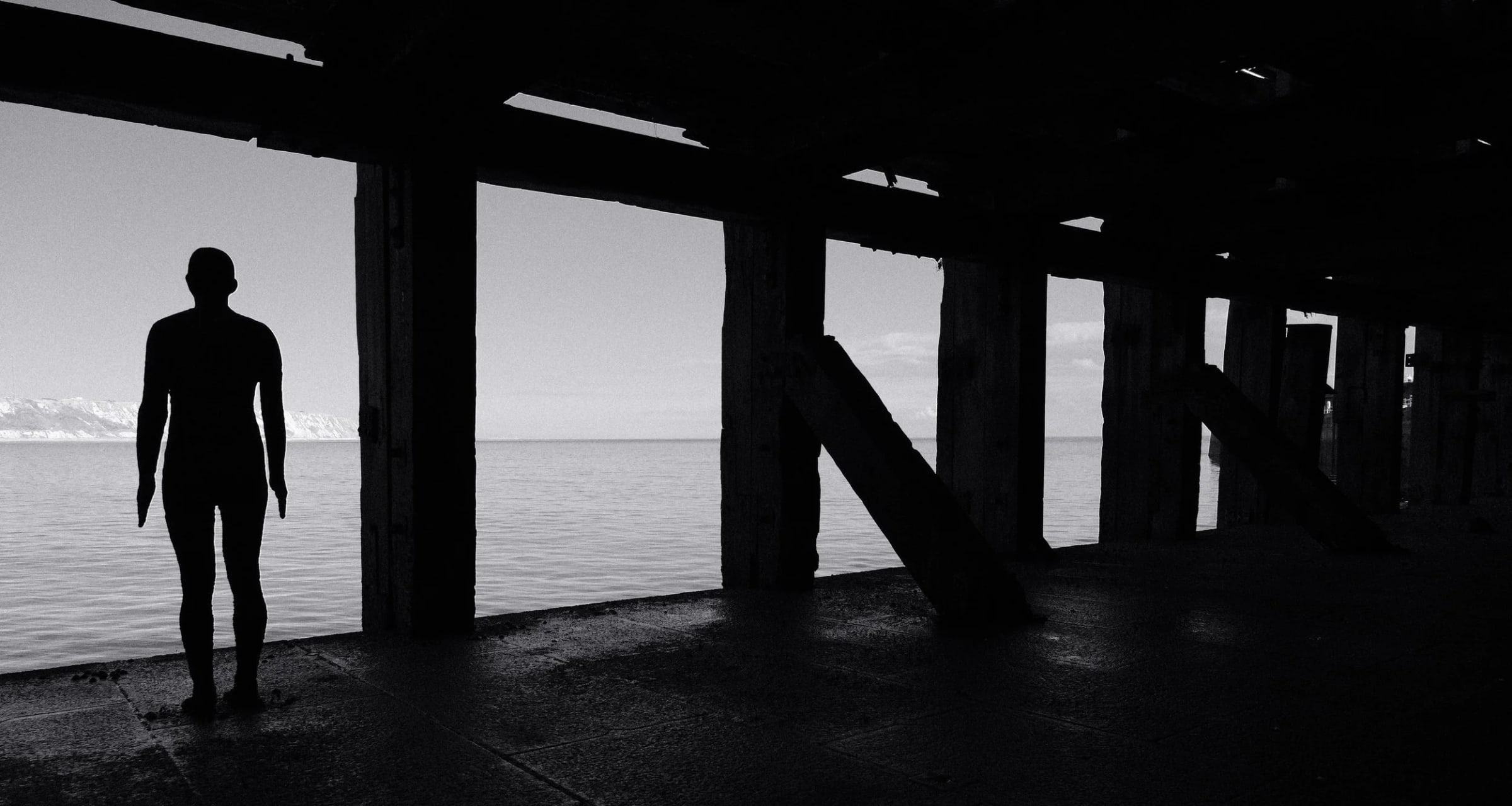 A black and white photo of the Antony Gormley Statue: Another Time XVIII (2013), at the Loading Bay underneath the Harbour Arm at Folkestone
