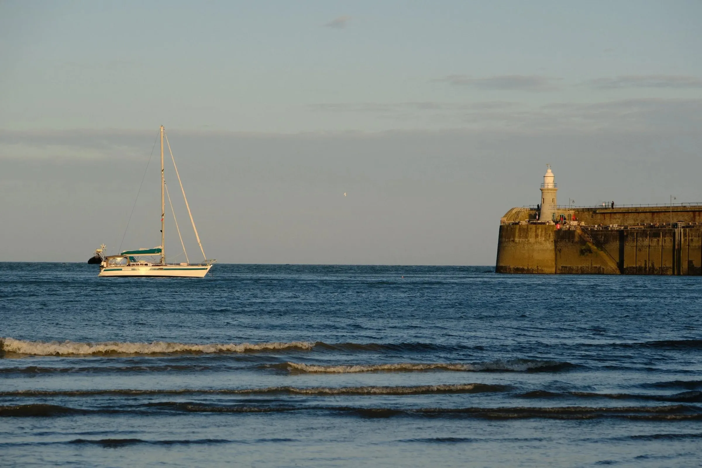 A boat drifts towards Folkestone Harbour Arm in calm evening water