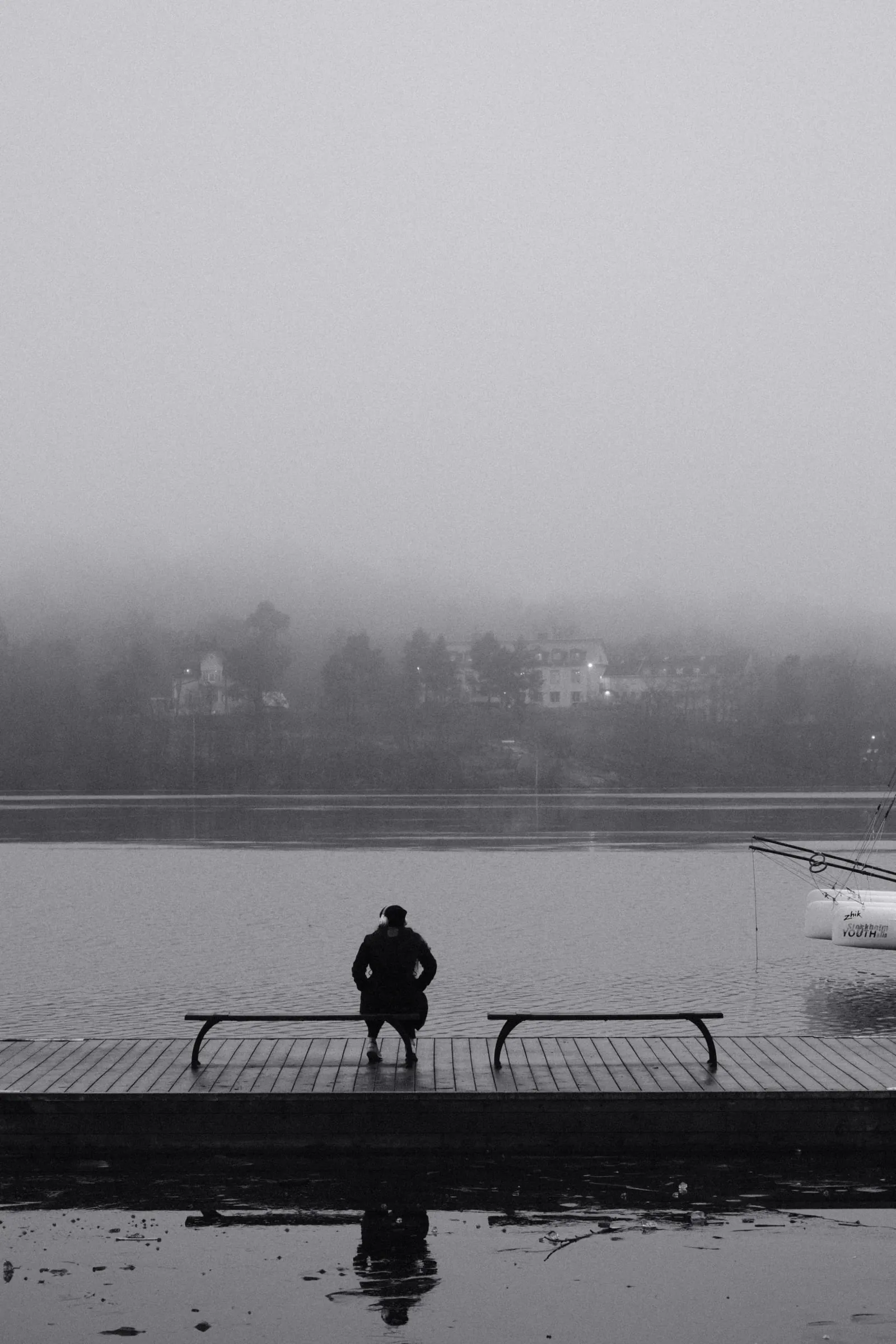 A woman sits at a bench looking across the water at Huvudsta Strand