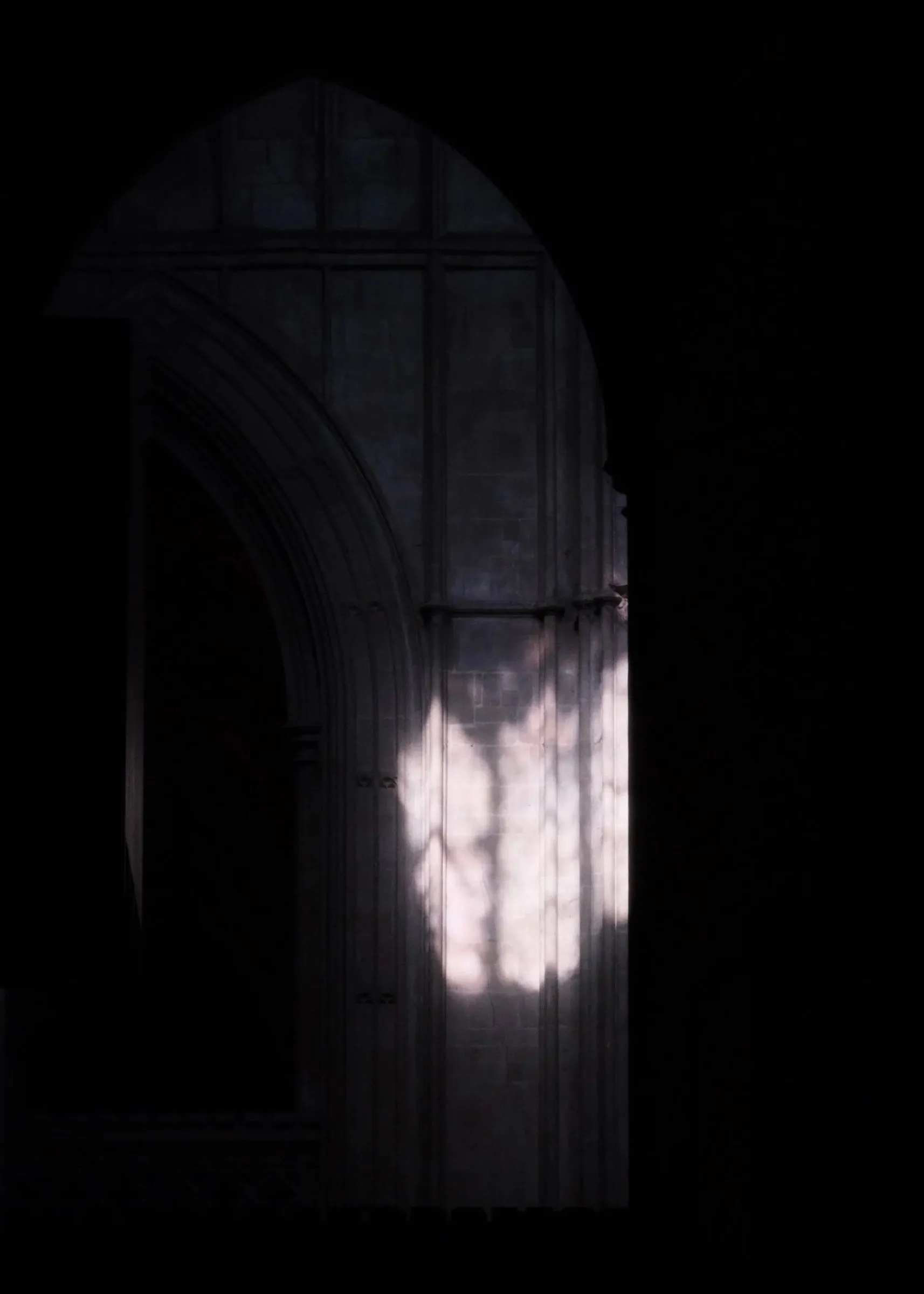 A patch of sunlight on stone inside a dark pointed arch