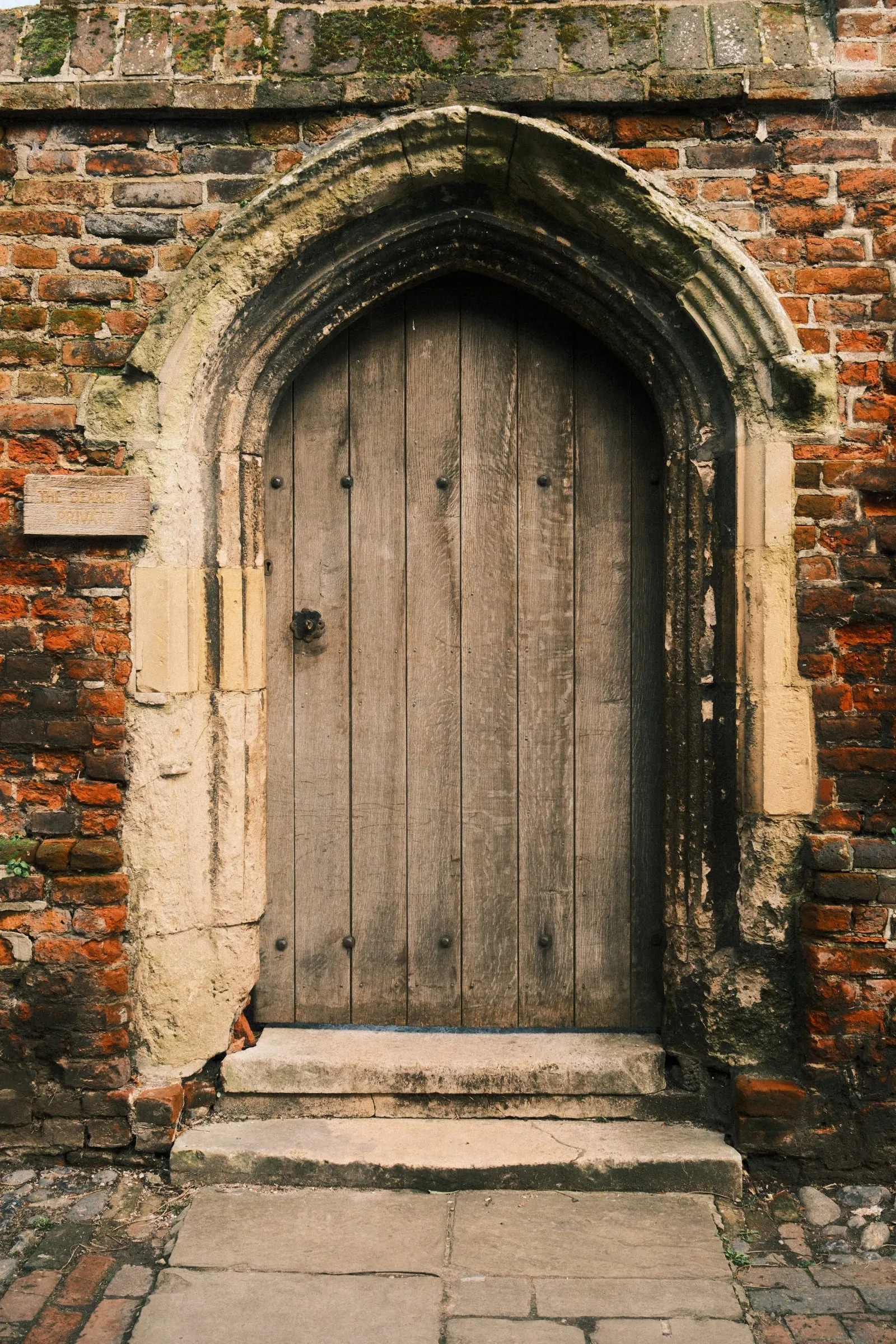An old wooden door set in a pointed stone arch in a brick wall