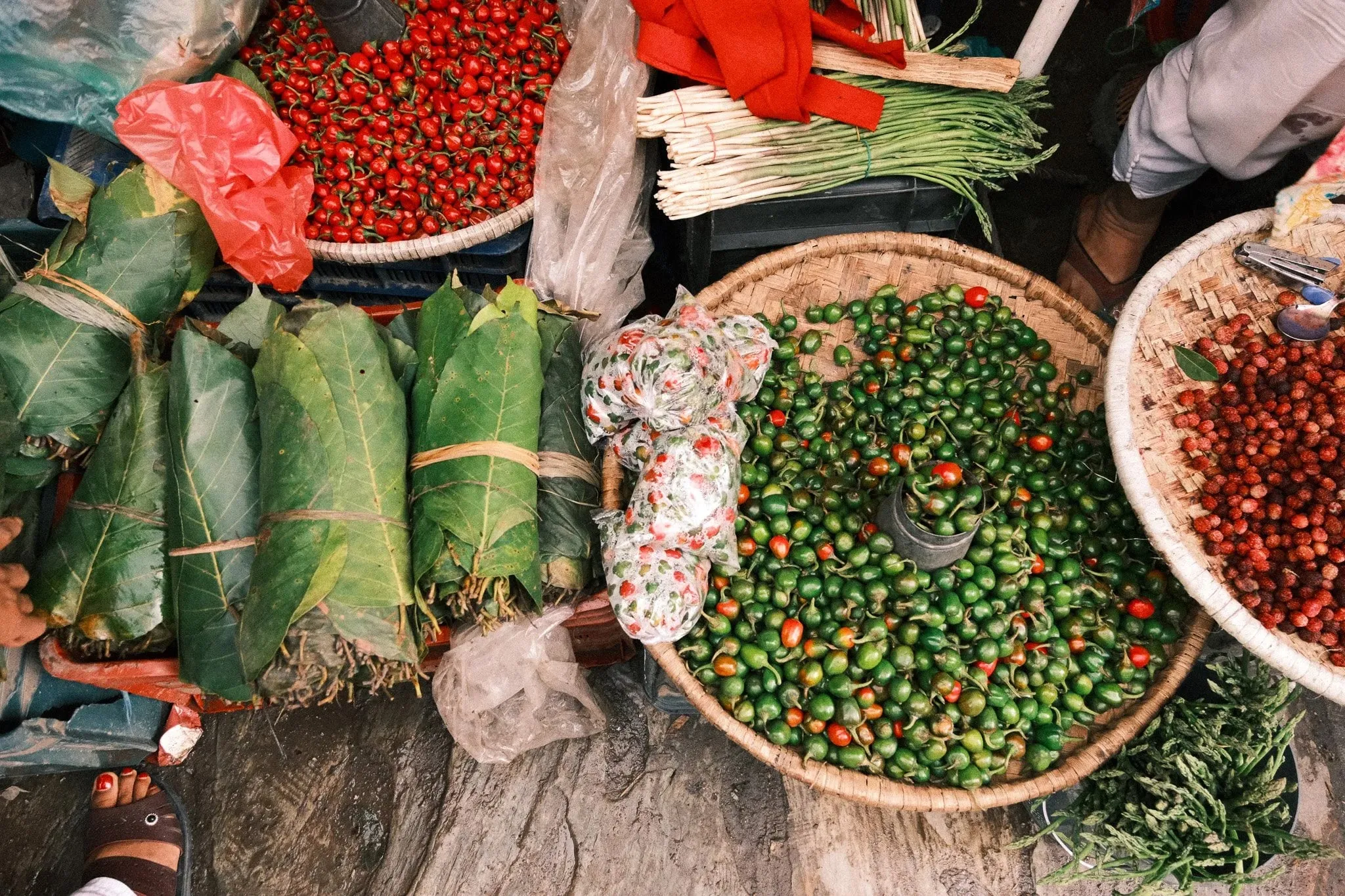 Baskets of green and red chillies and bundles of leaves at a market stall seen from above
