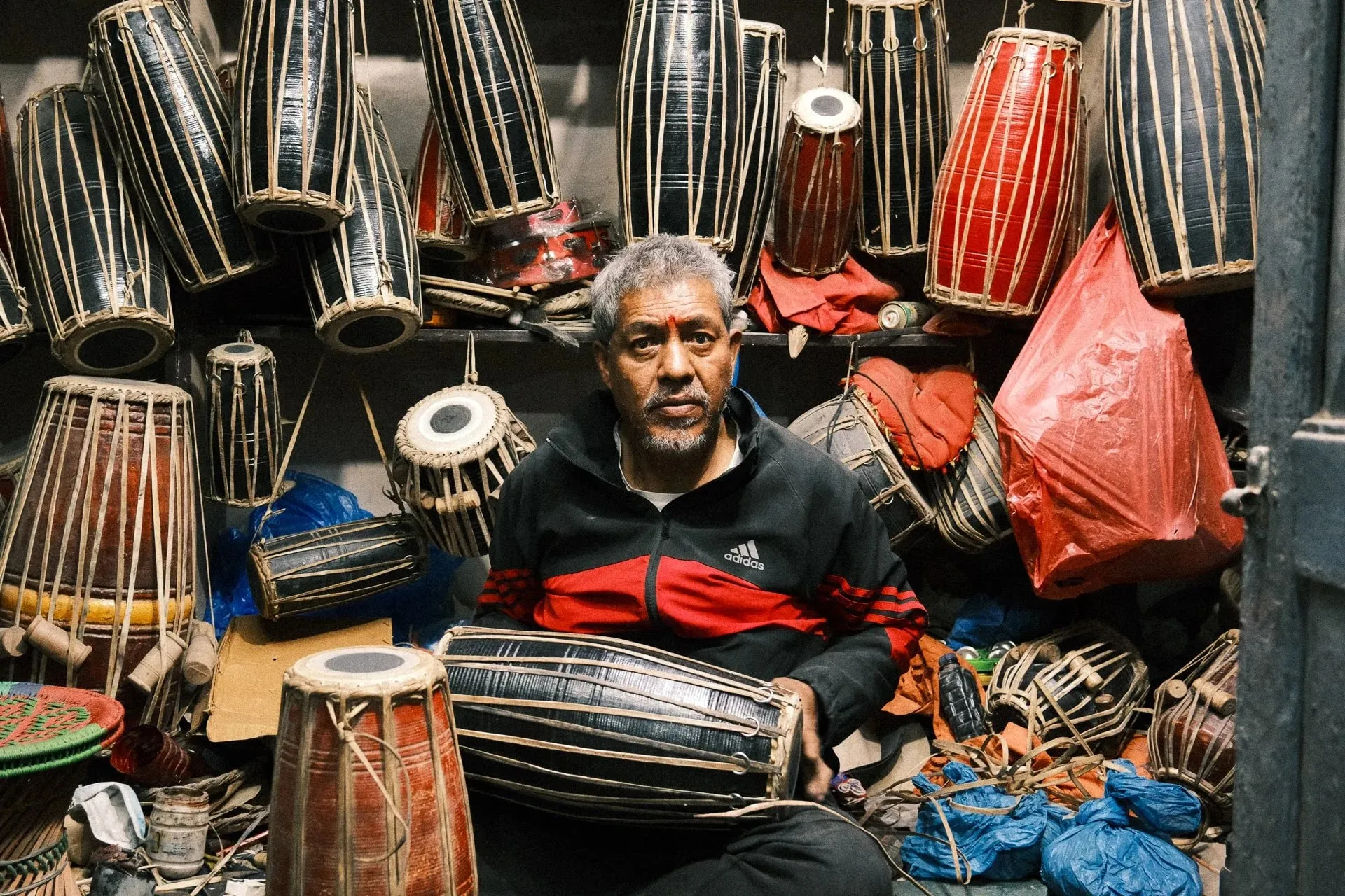 A man sitting among hanging drums in his shop