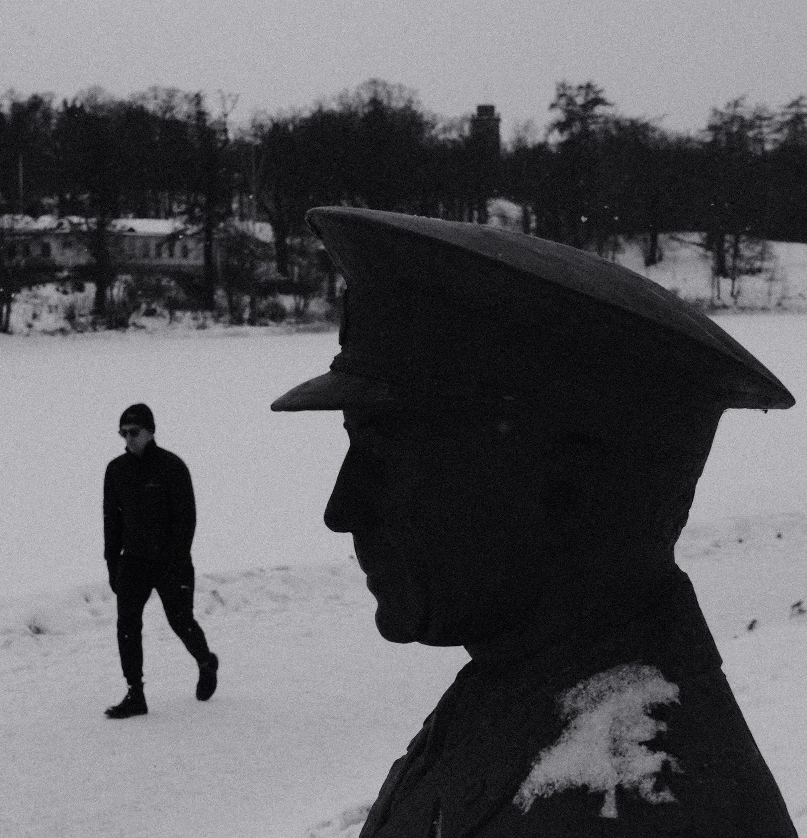 Black and white photo of a man walking past a statue at Djurgården, Stockholm