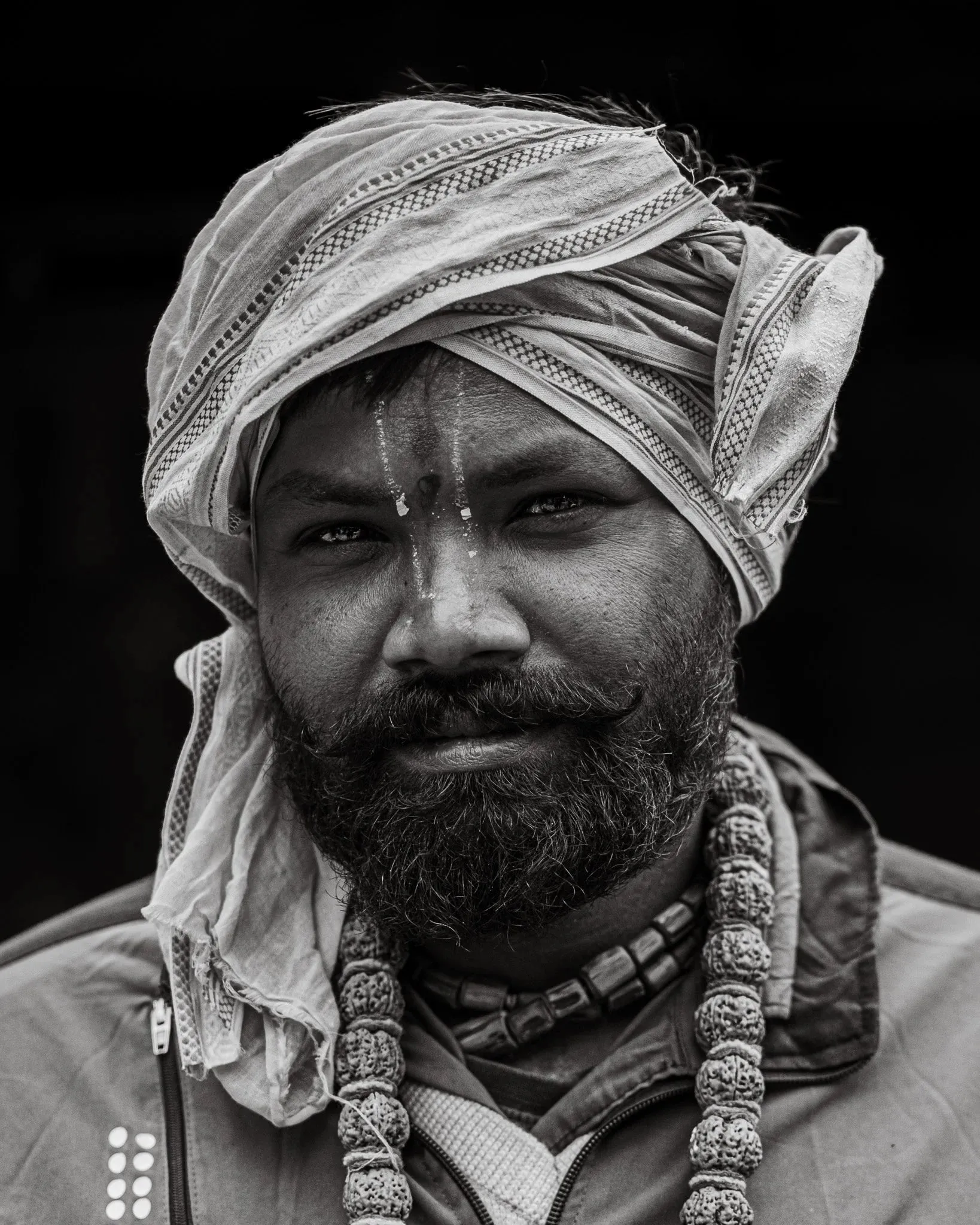 Black and white portrait of a bearded sadhu wearing a wrapped head covering and necklaces at Muktinath, Mustang, Nepal.
