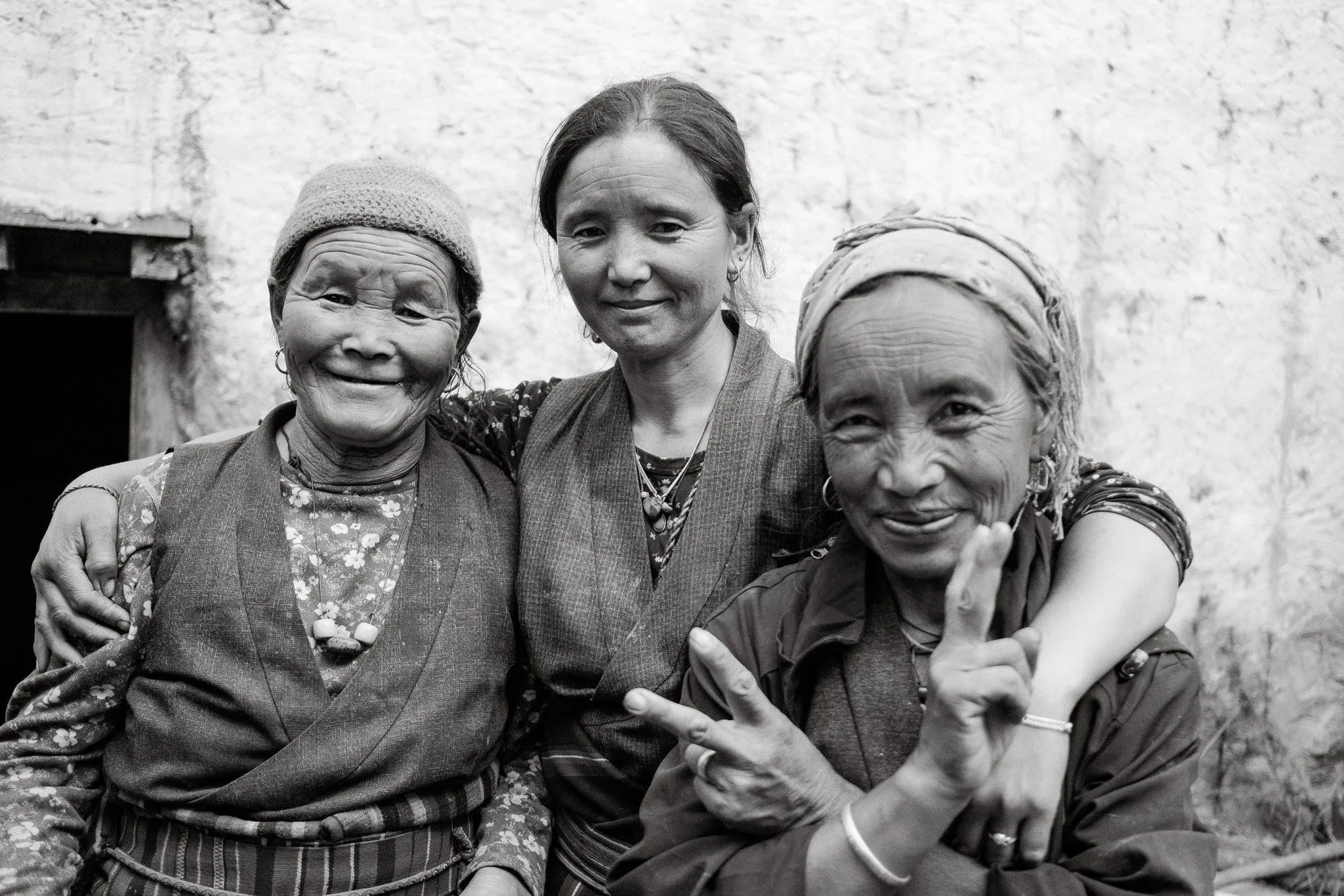 Black and white portrait of three women posing together, one making a peace sign, in Dhakmar, Upper Mustang, Nepal.