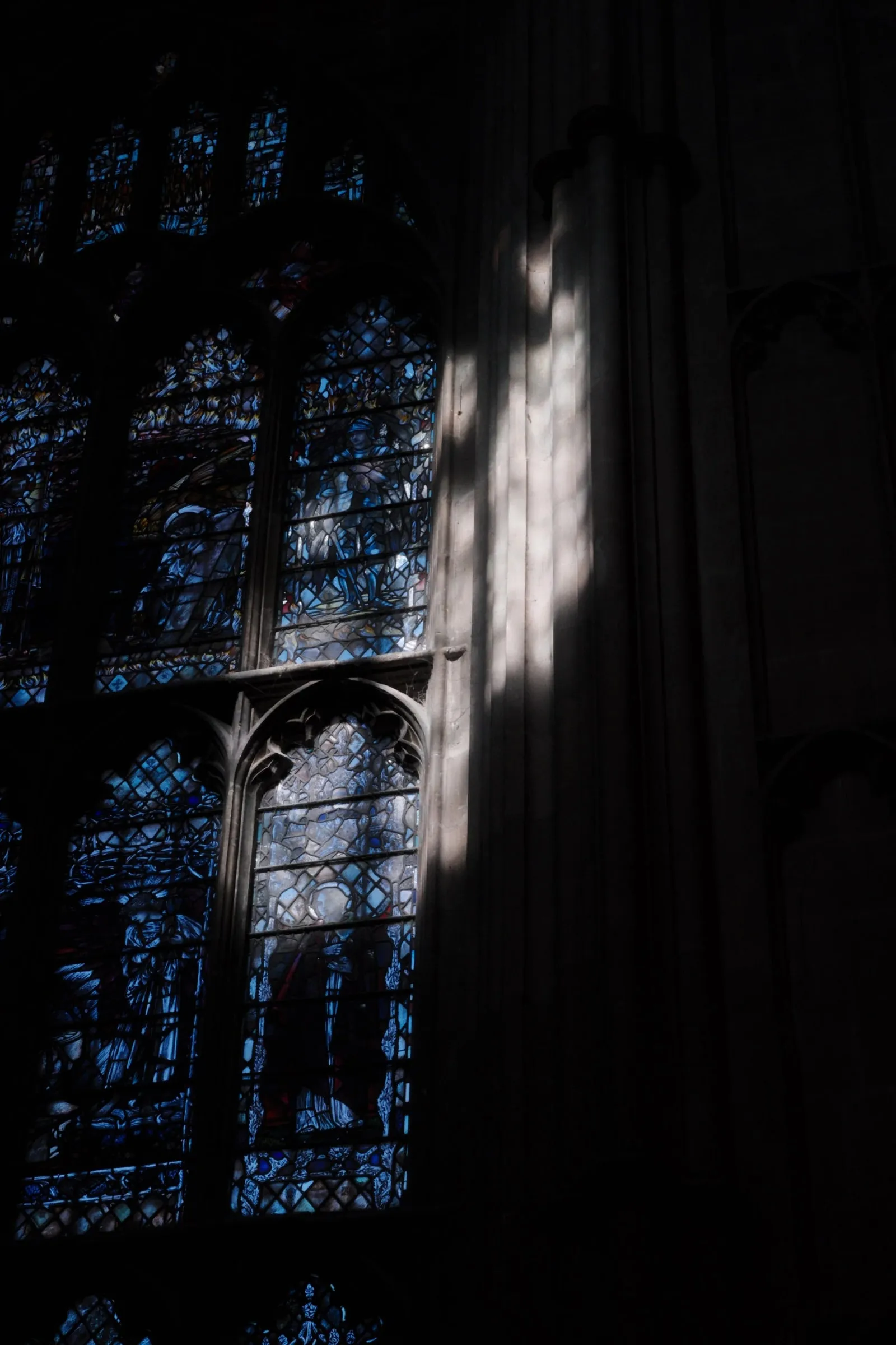 Light falling on a pillar beside deep blue stained glass windows