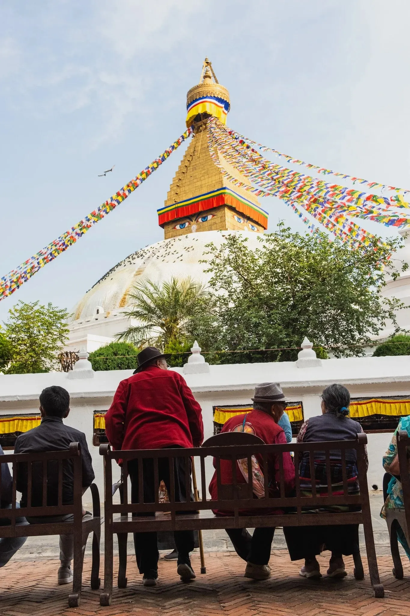 People sitting on benches in front of the Boudhanath stupa and its prayer flags