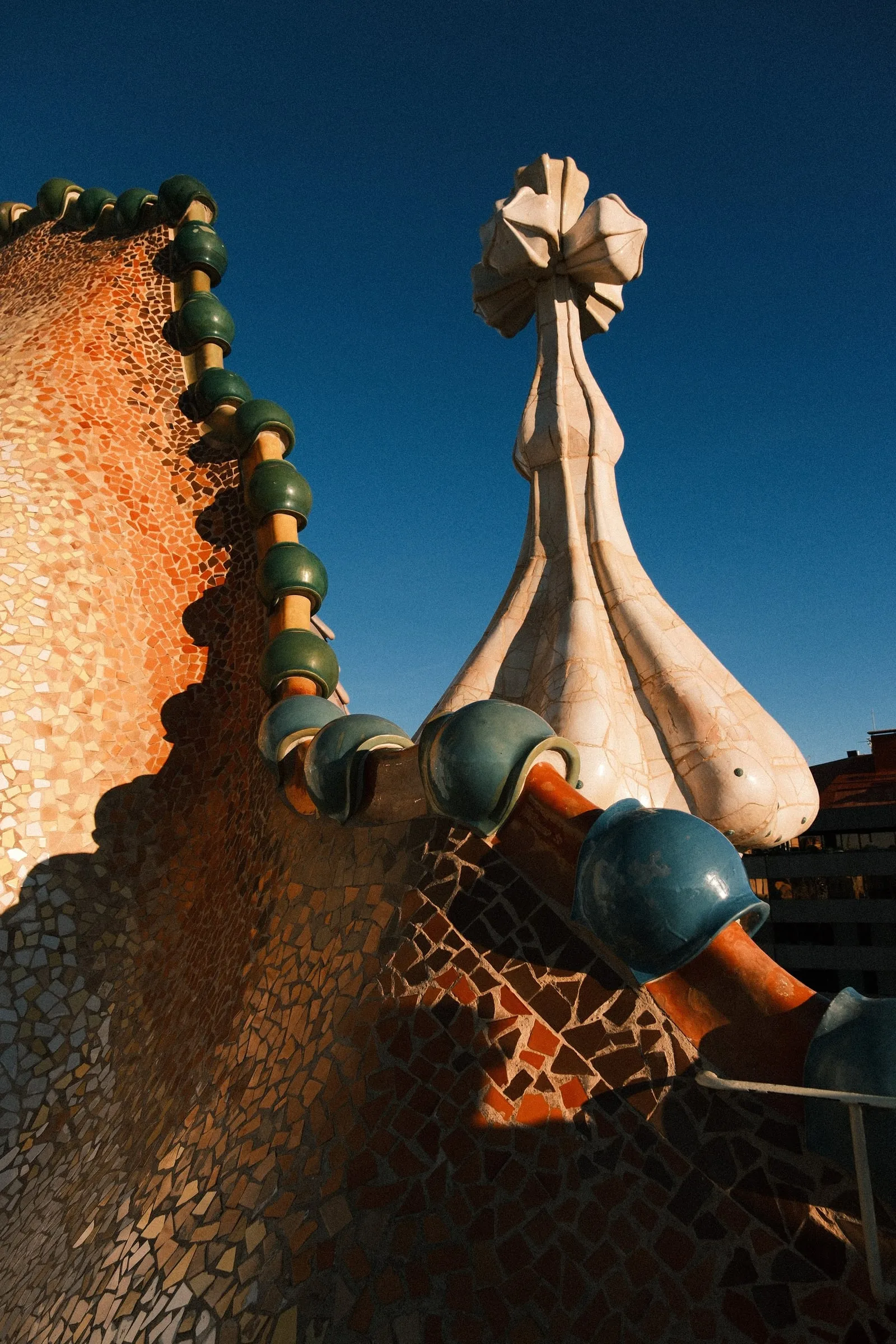The mosaic-tiled roof and a chimney of Casa Batlló against a deep blue sky