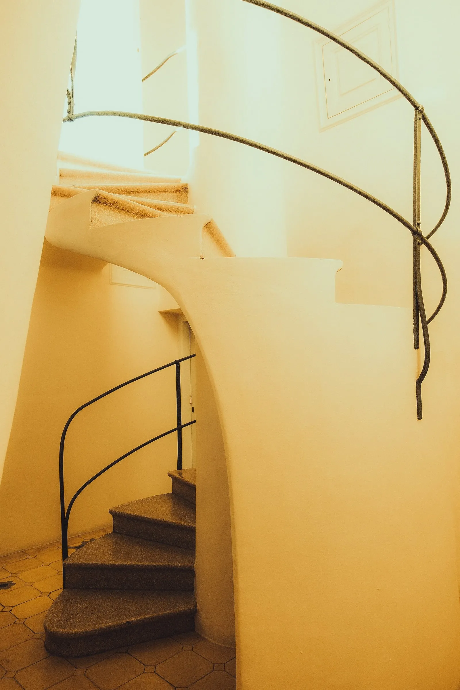 A spiral staircase with a curving metal handrail in warm light inside Casa Batlló