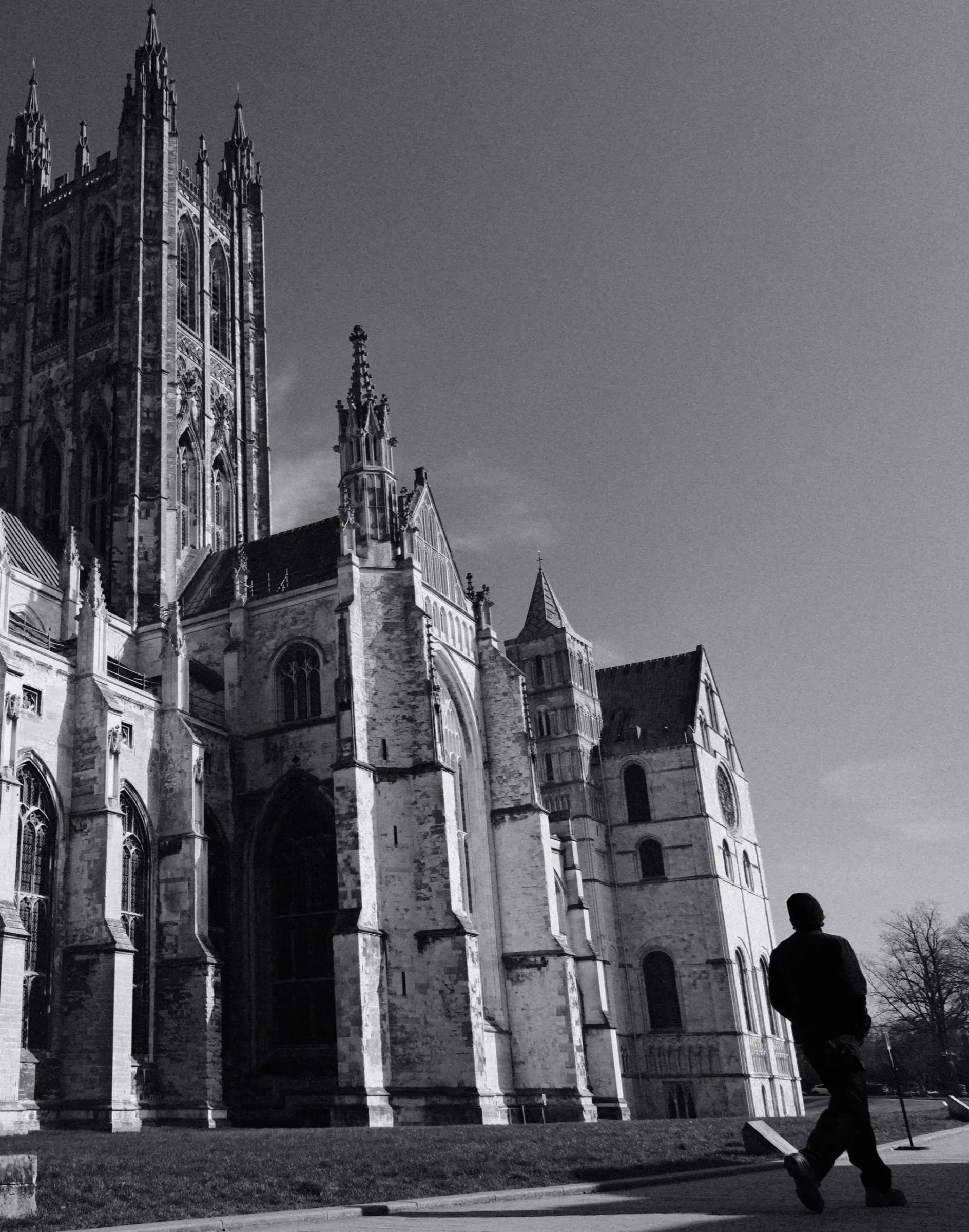 Black and white photo of a person walking past Canterbury Cathedral in bright sun