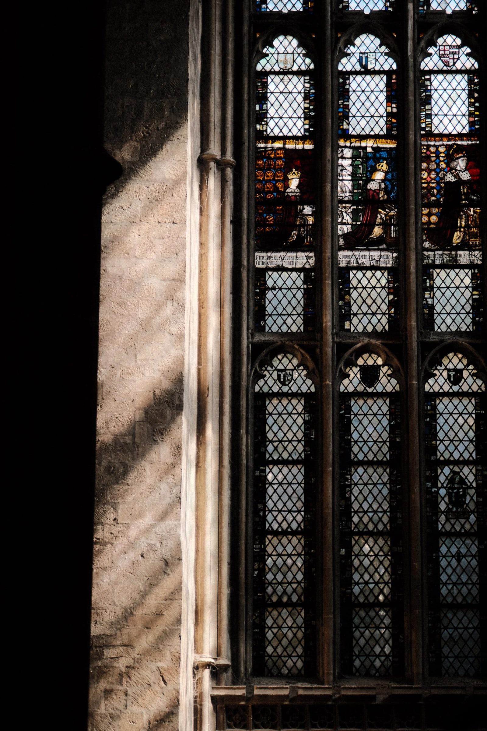 Sunlight falling across stone beside a tall stained glass window at Canterbury Cathedral