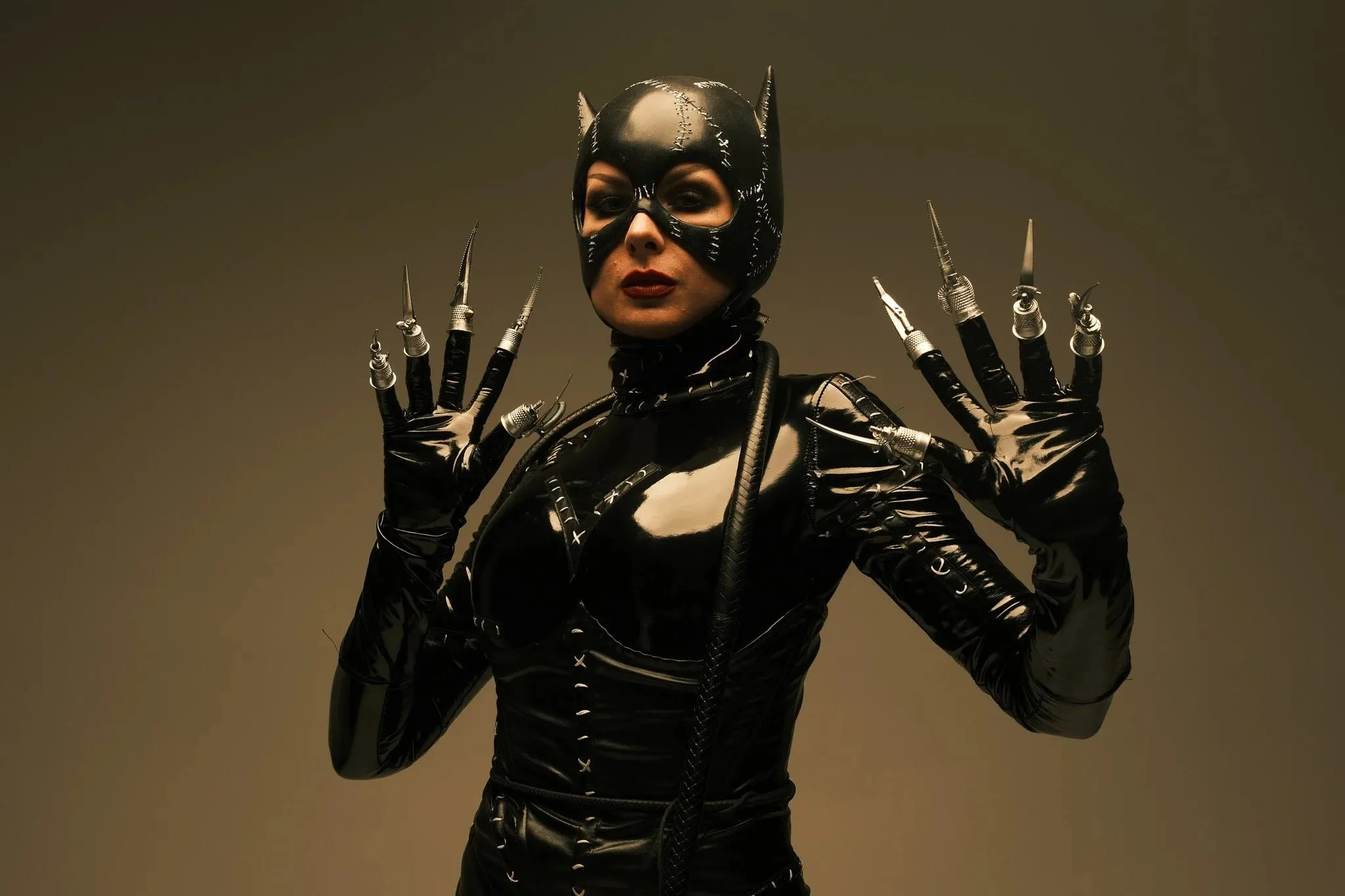 A model in a Catwoman costume with long claws, posing against a brown backdrop