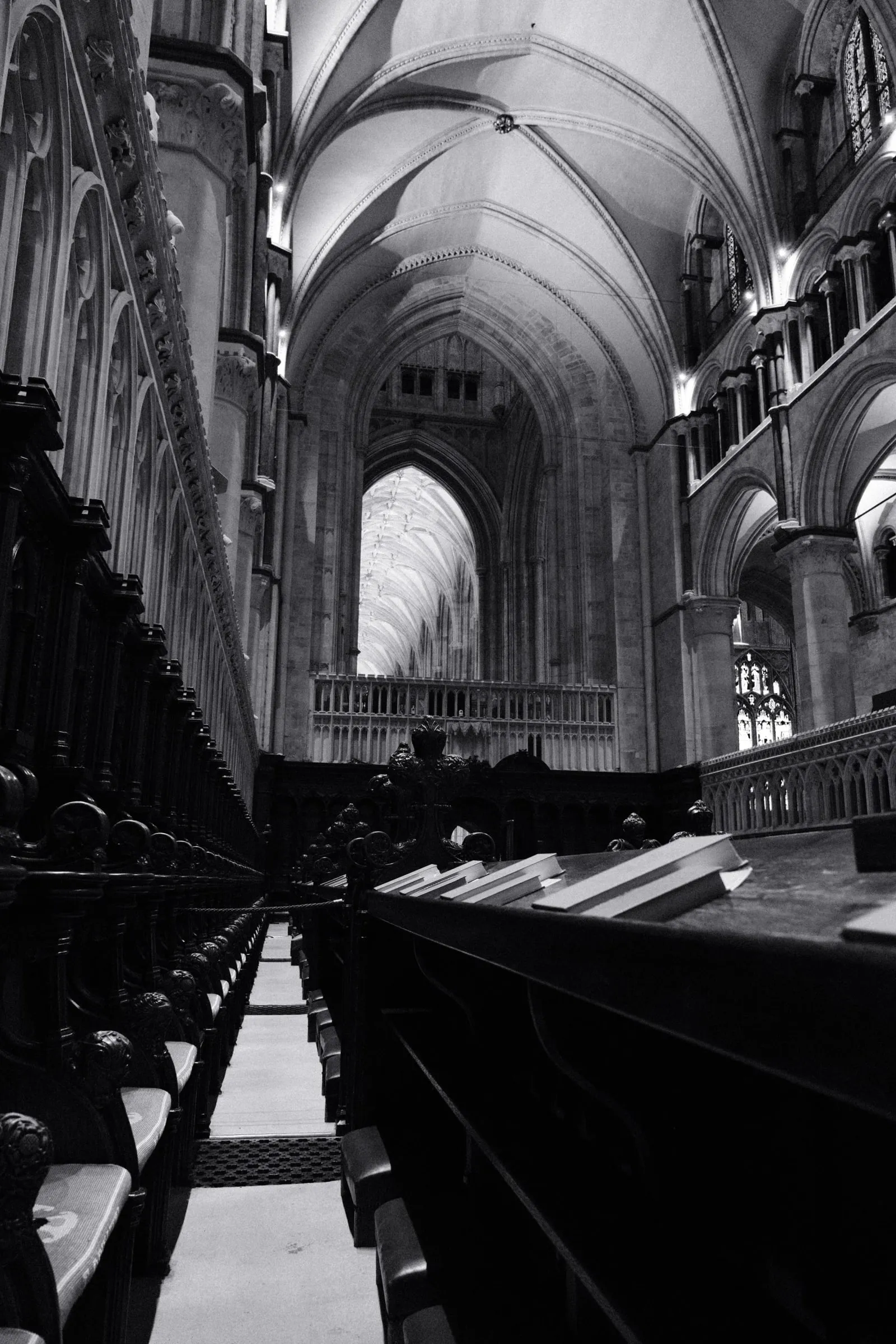 Black and white photo of rows of wooden choir stalls beneath high vaulting