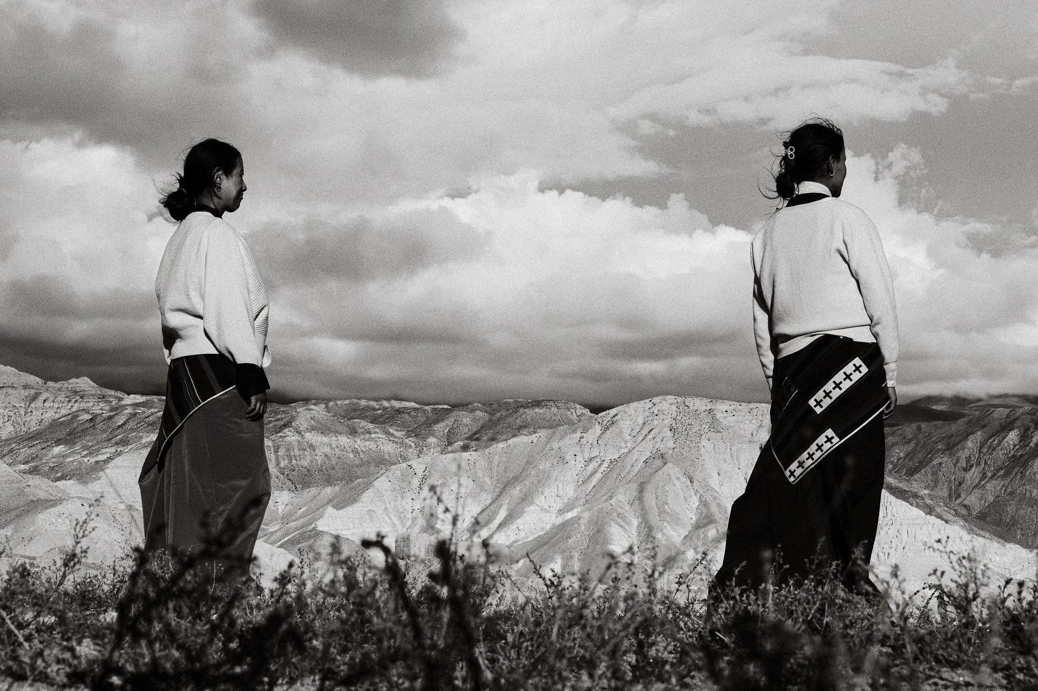 Black and white photo of two women in traditional dress looking out over the hills near Choser