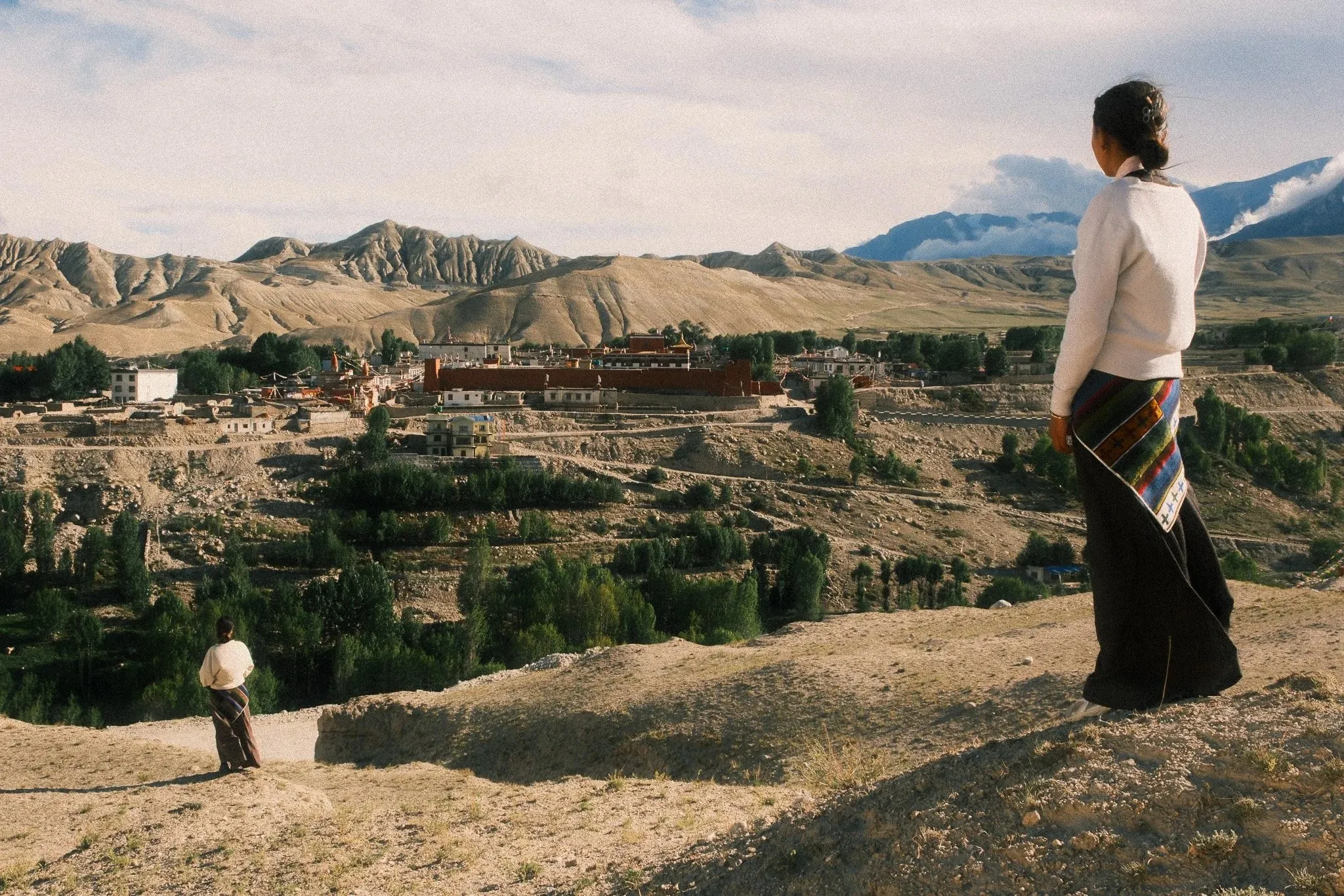 A woman in traditional dress looking out over a village and fields near Choser