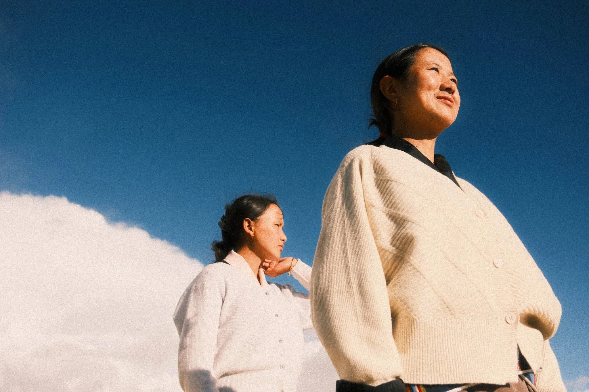 Two young women in cream jackets against a deep blue sky with clouds