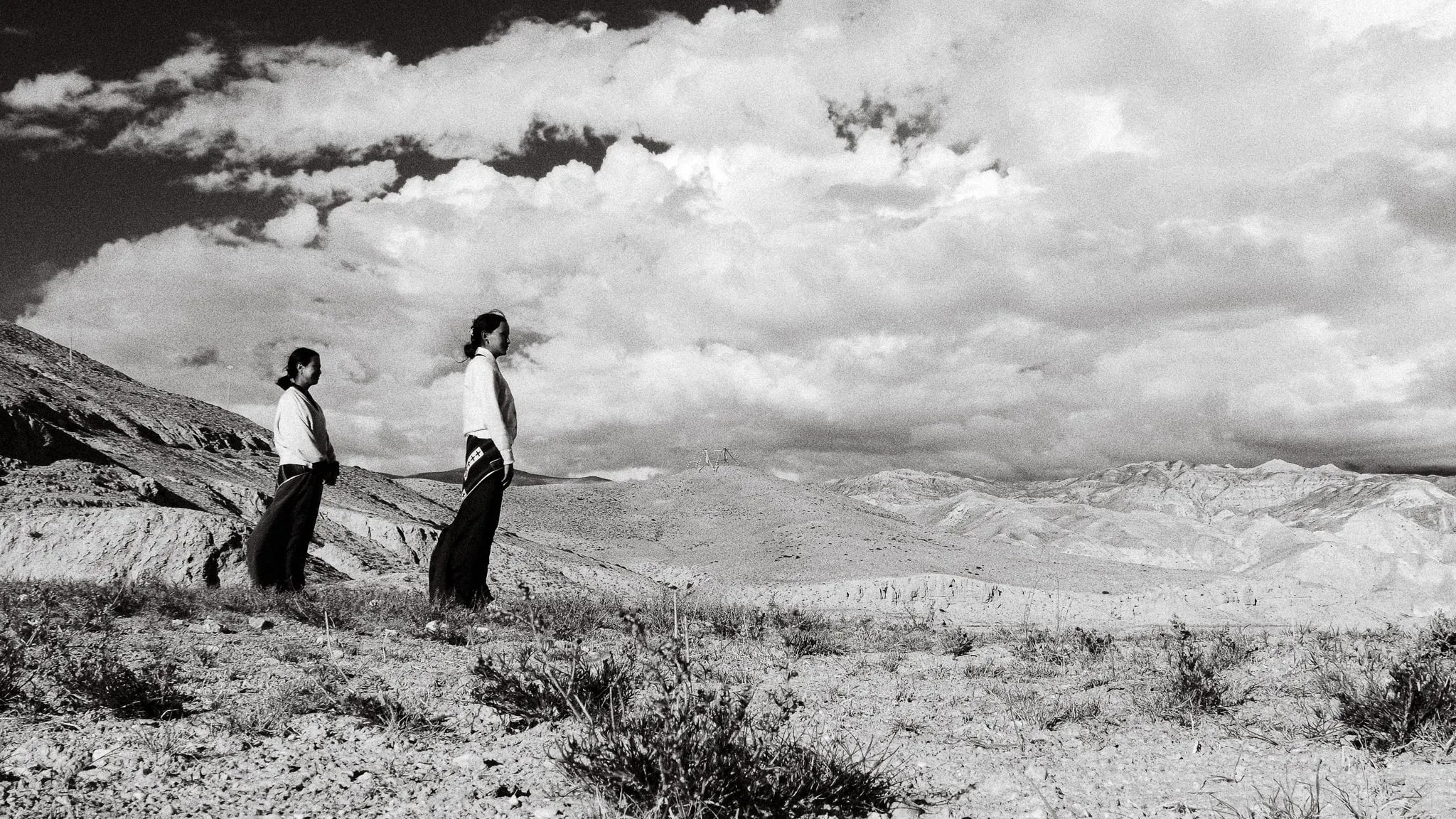 Black and white photo of two women standing on a hillside under large clouds near Choser
