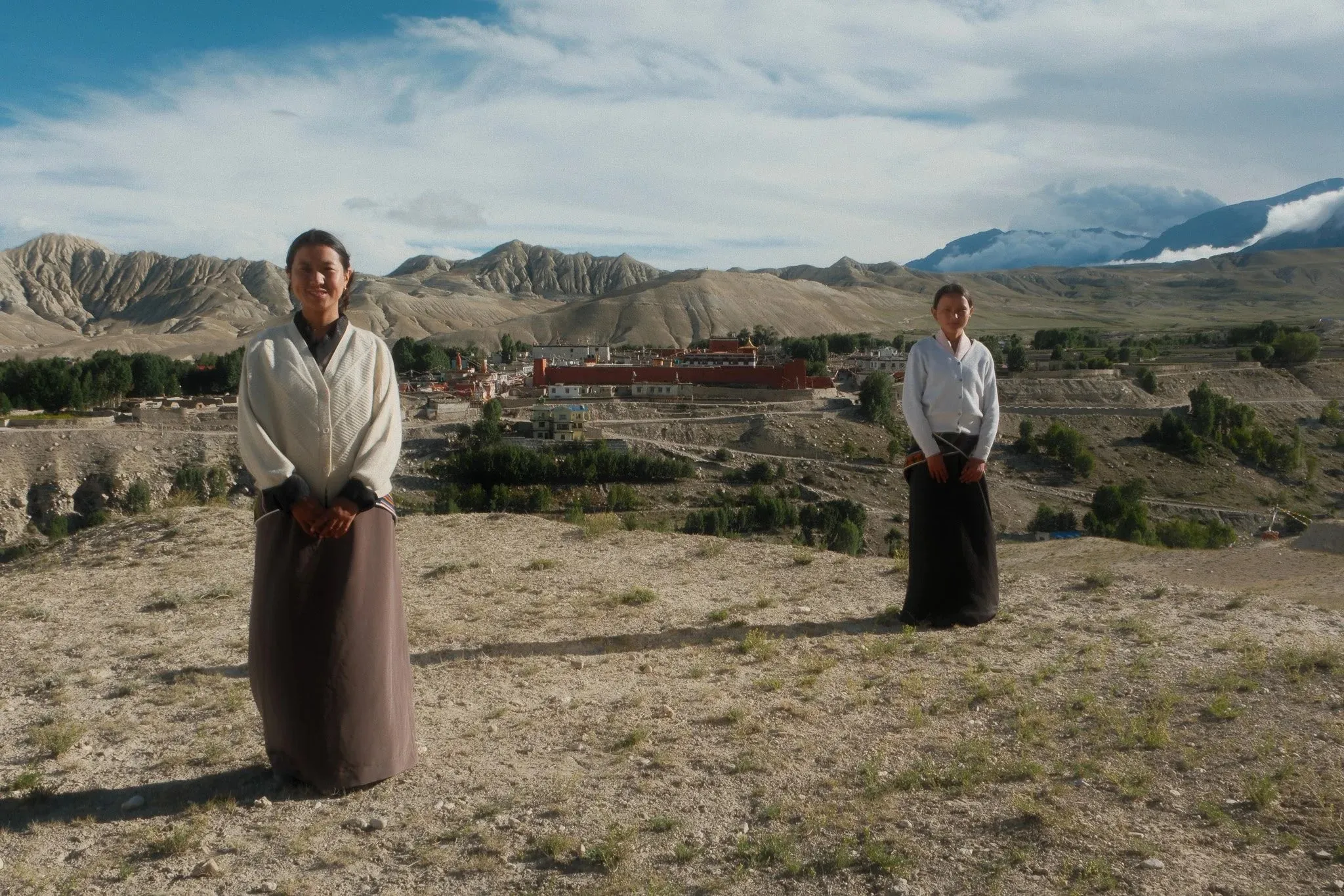 Two women in traditional dress standing on a hillside above a village near Choser