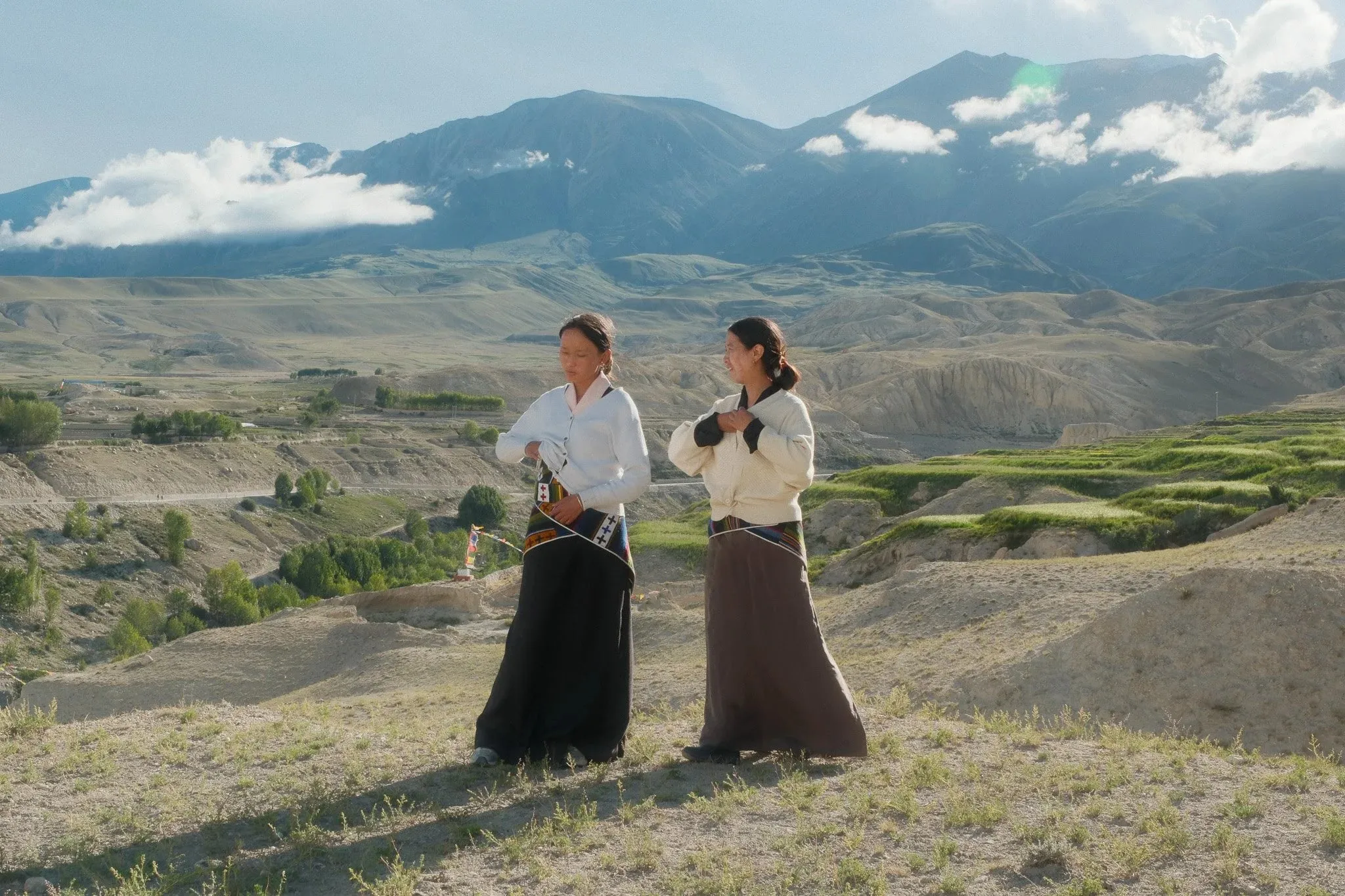 Two women in traditional dress talking on a hillside above green fields near Choser