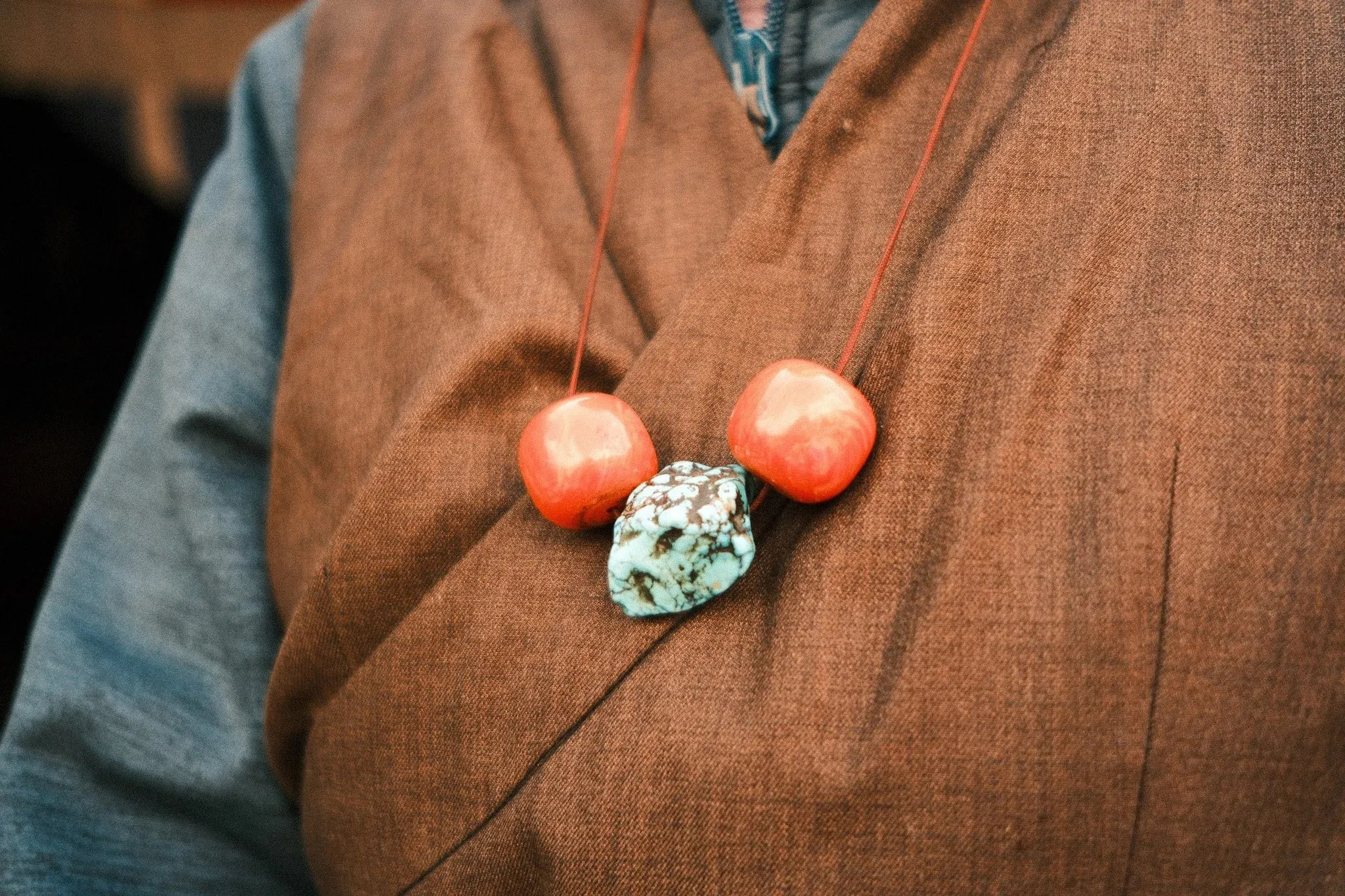 Coral and turquoise beads on a necklace against a brown wrap dress
