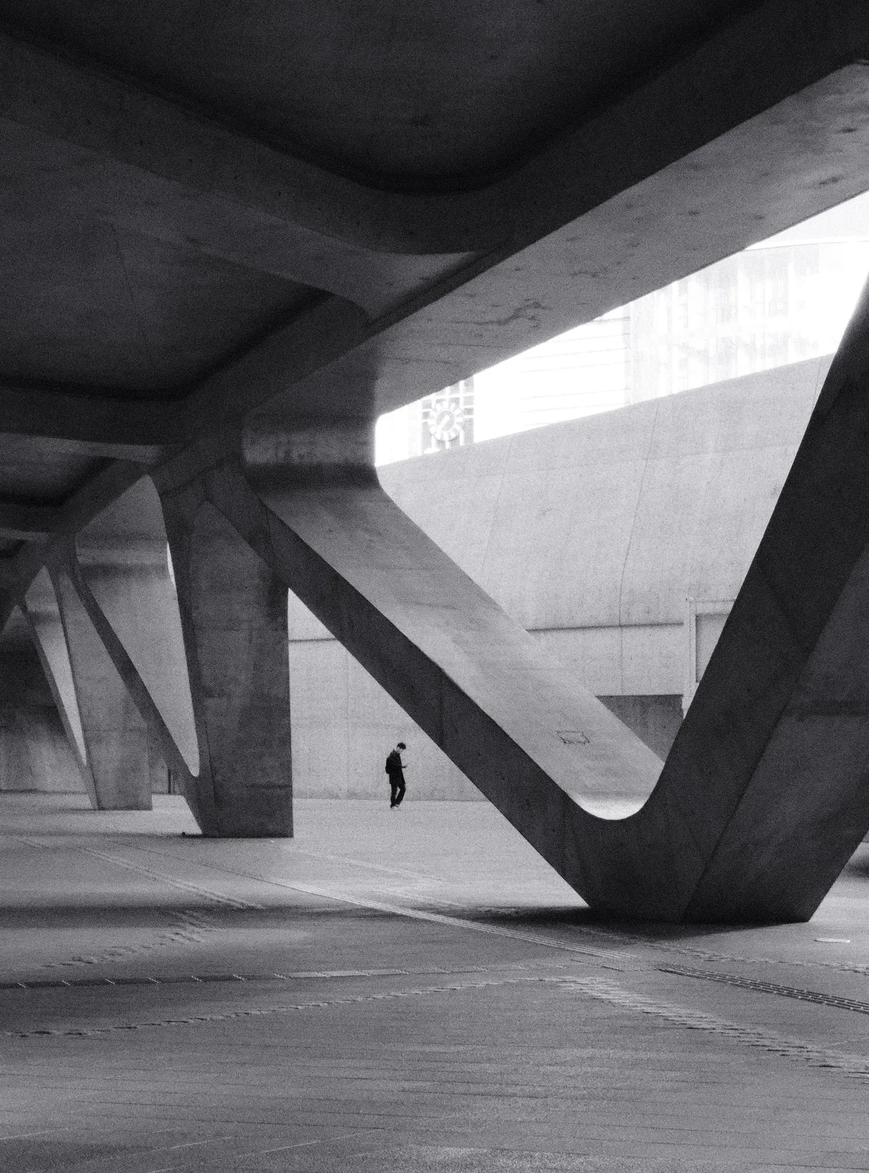 A lone person walks beneath the angled concrete pillars of Dongdaemun Design Plaza