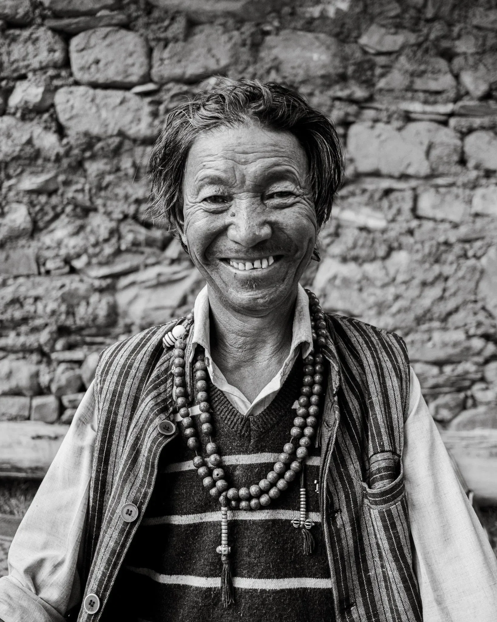 Black and white portrait of a smiling man wearing prayer beads in Dhakmar