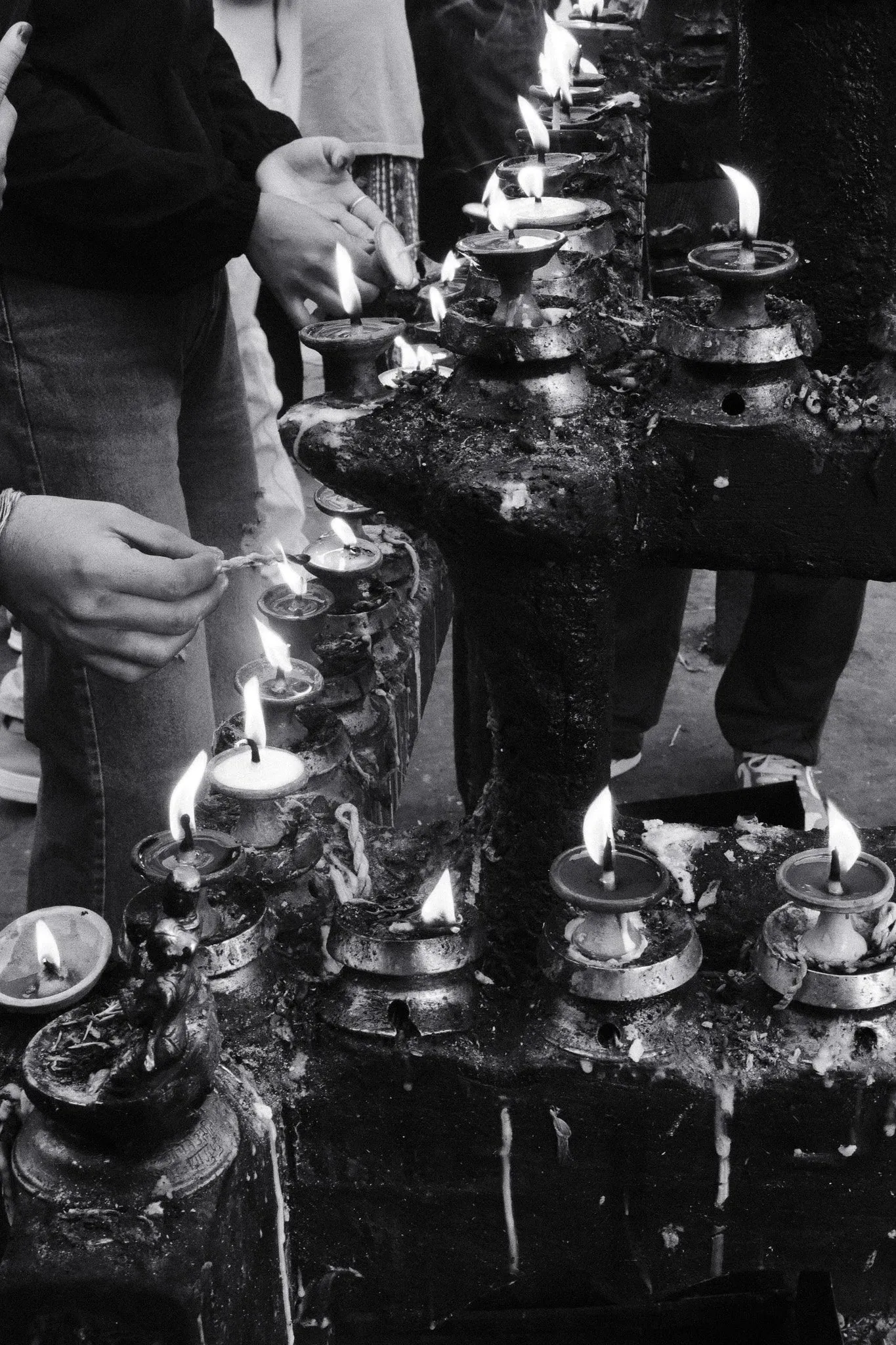 Black and white photo of hands lighting butter lamps at a shrine