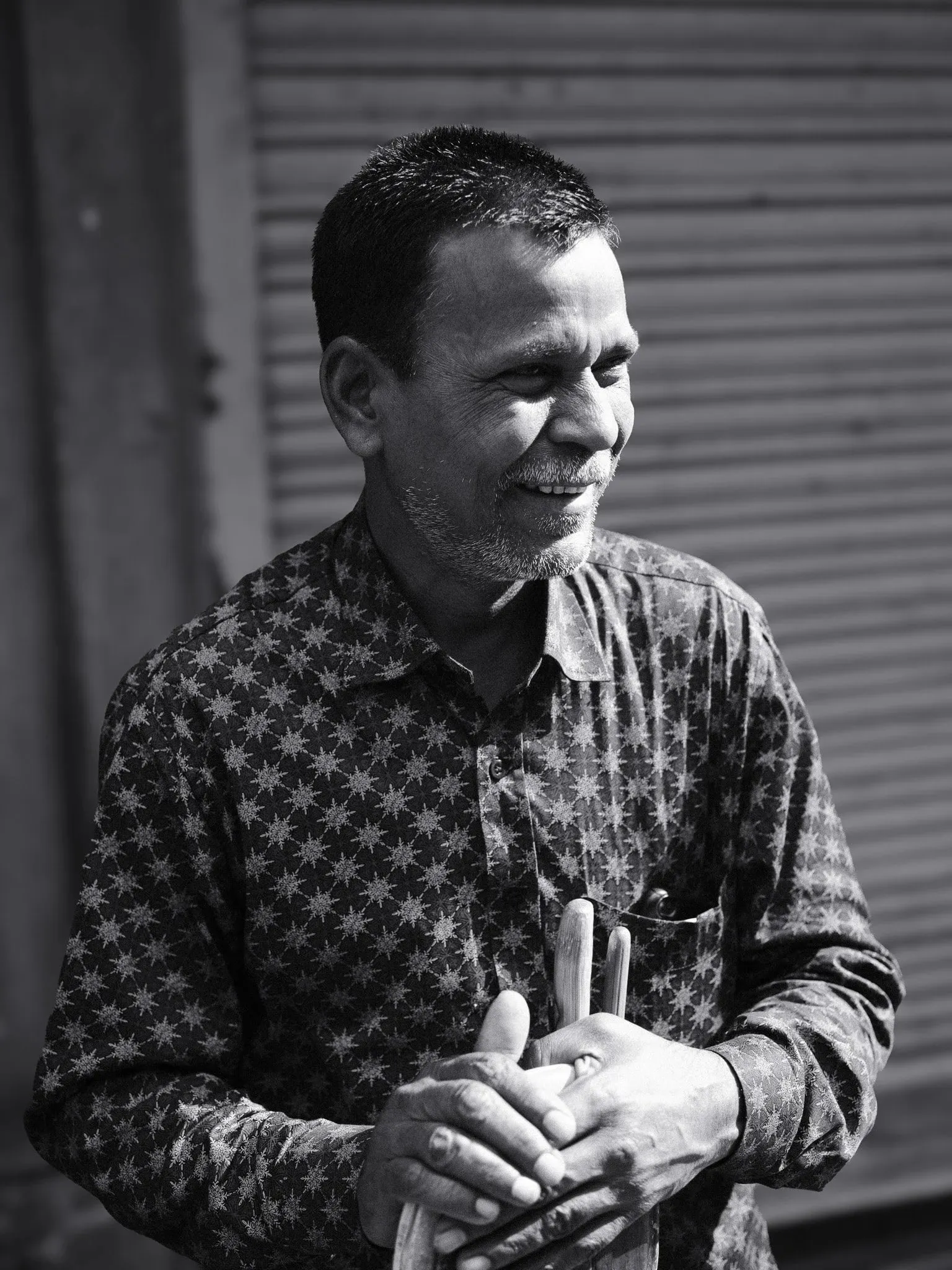 Black and white portrait of a man in a patterned shirt, smiling and looking away