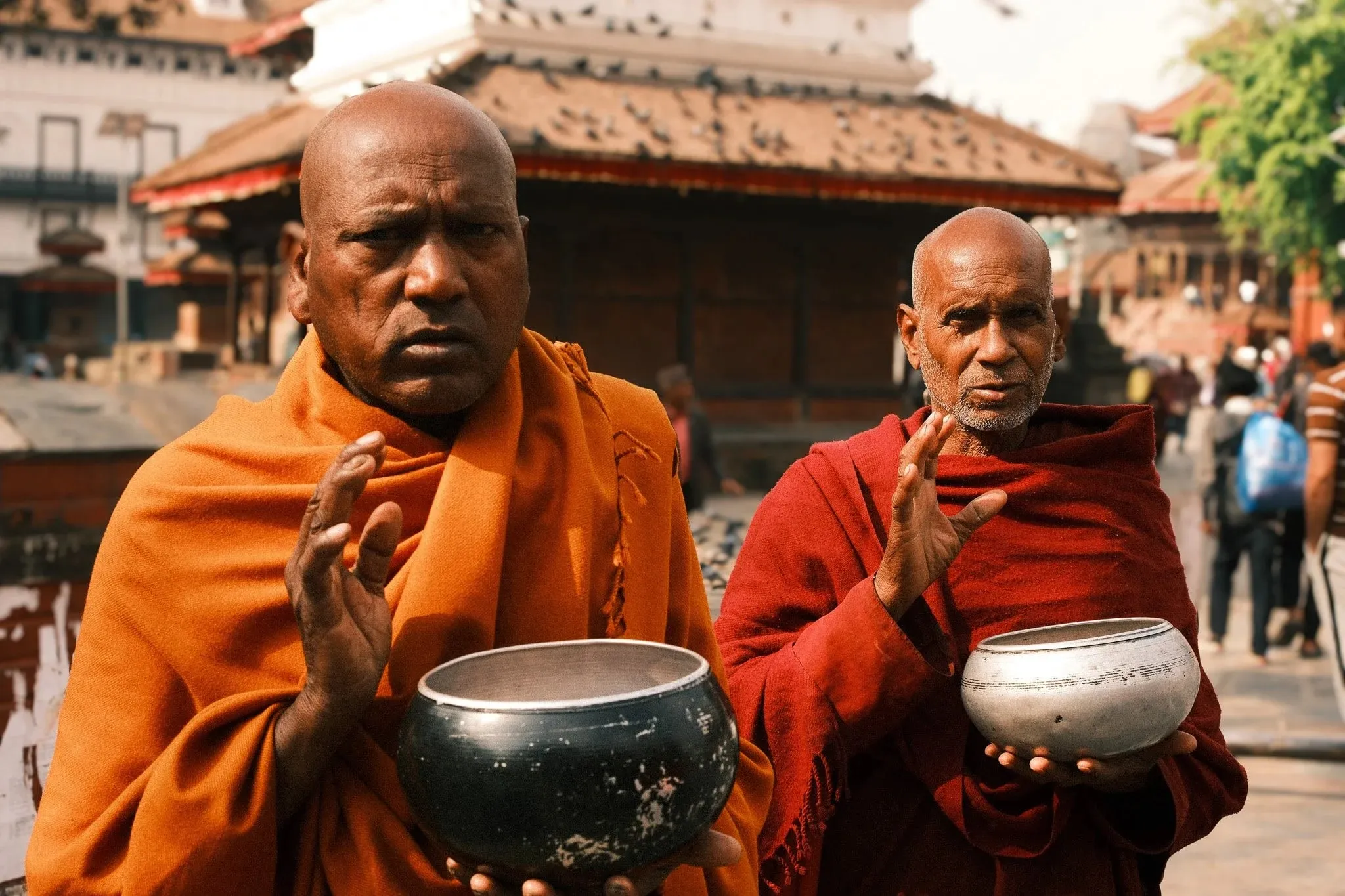 Two men in orange and red robes holding alms bowls in Kathmandu Durbar Square
