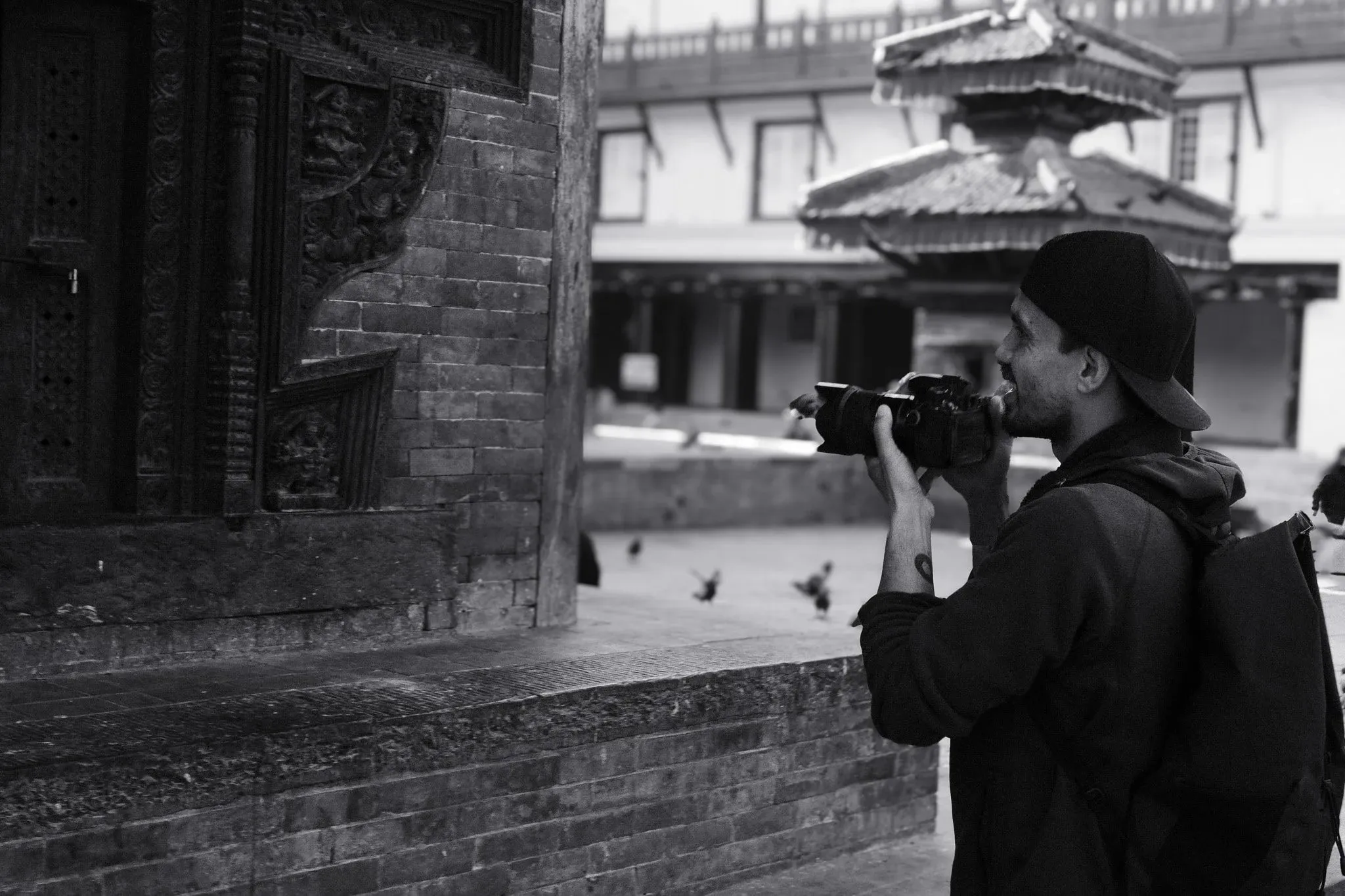 Black and white photo of a photographer with his camera beside a temple wall