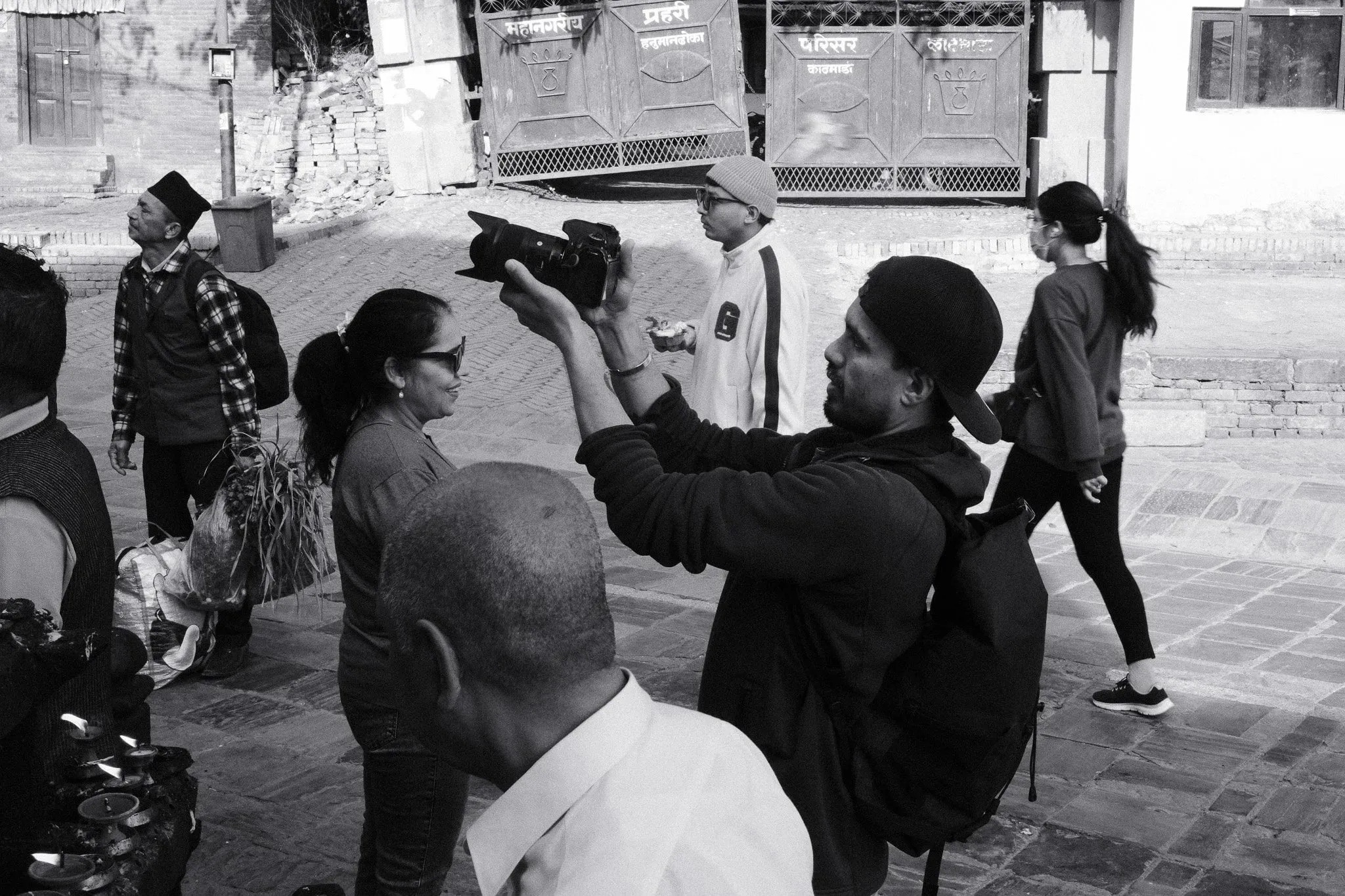 Black and white photo of a photographer raising his camera among people in the square
