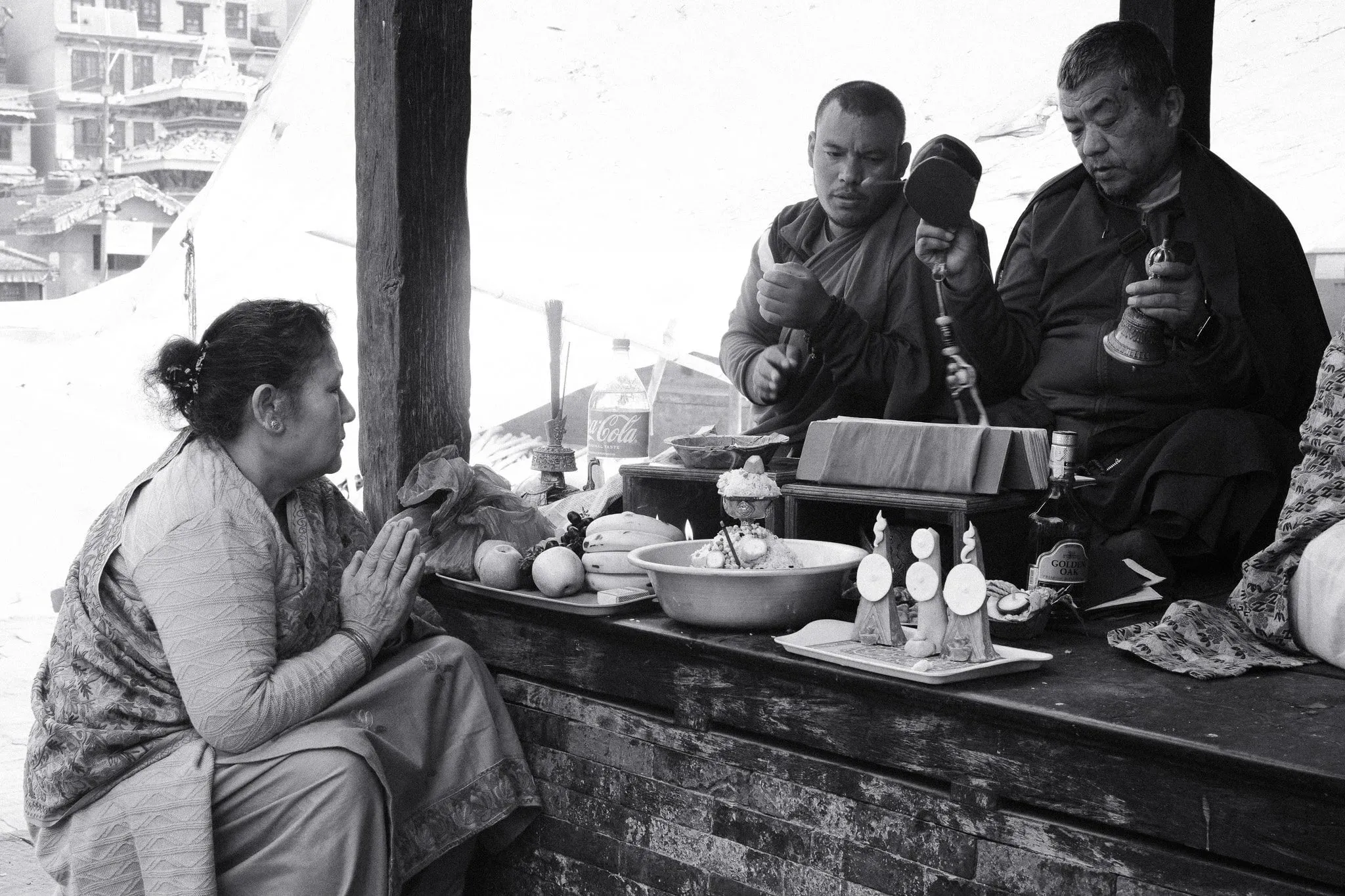 Black and white photo of a woman praying in front of two men with offerings at a shrine