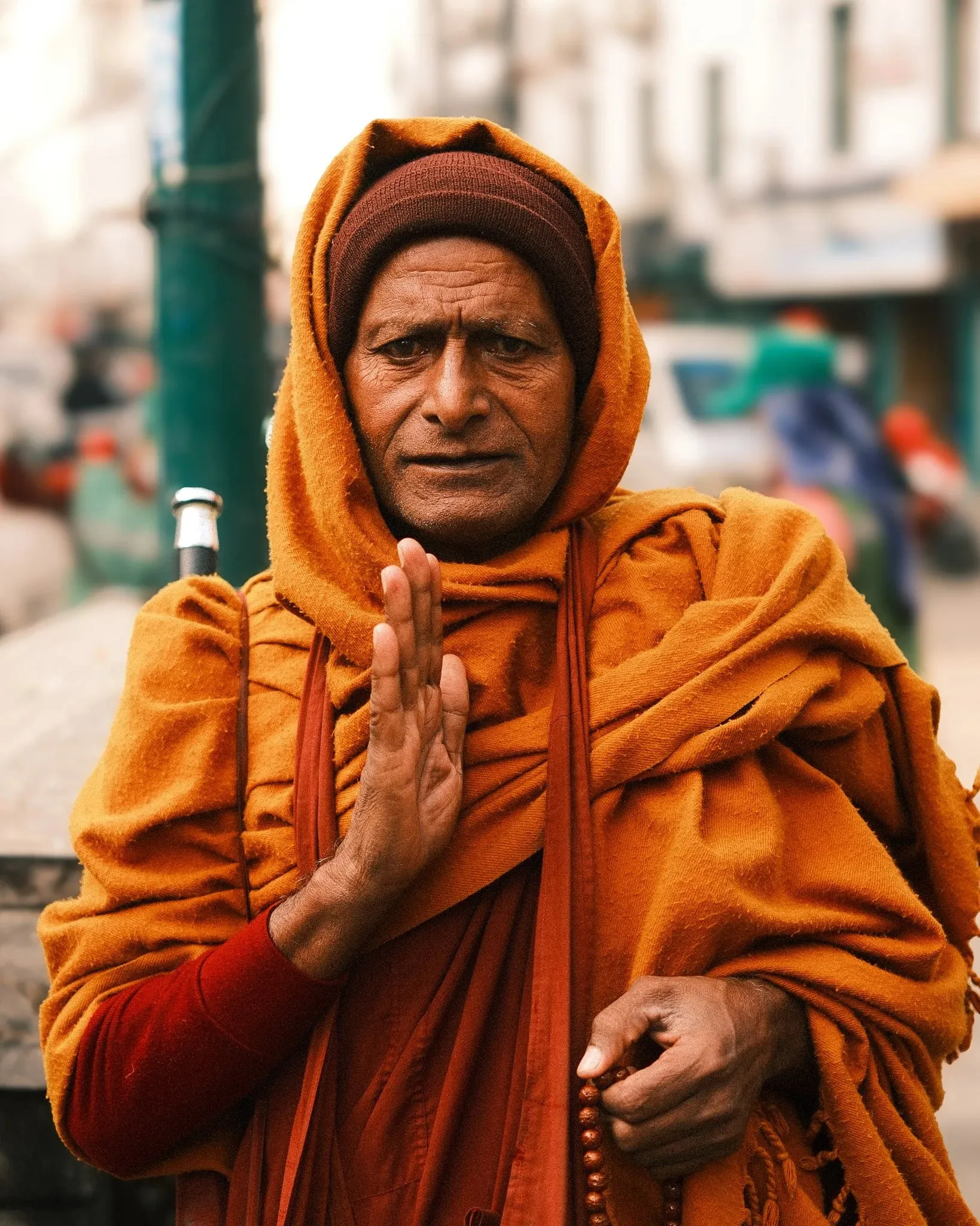 An older man wrapped in orange cloth holding prayer beads and raising his hand