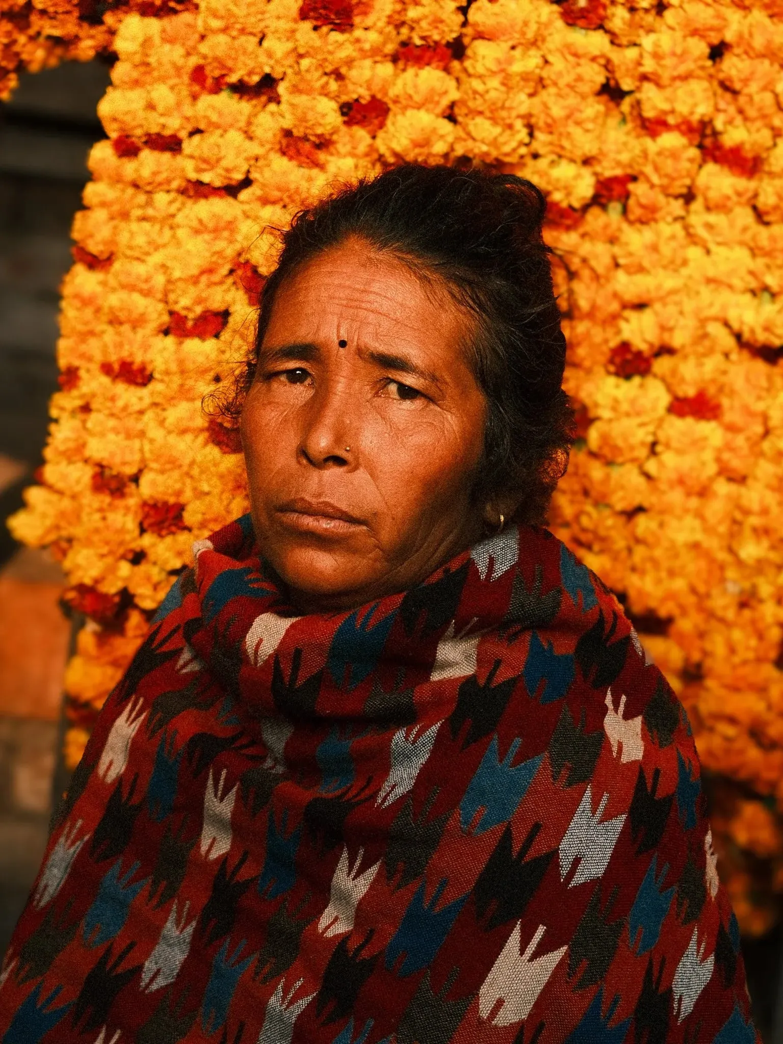 A woman in a patterned shawl in front of hanging marigold garlands