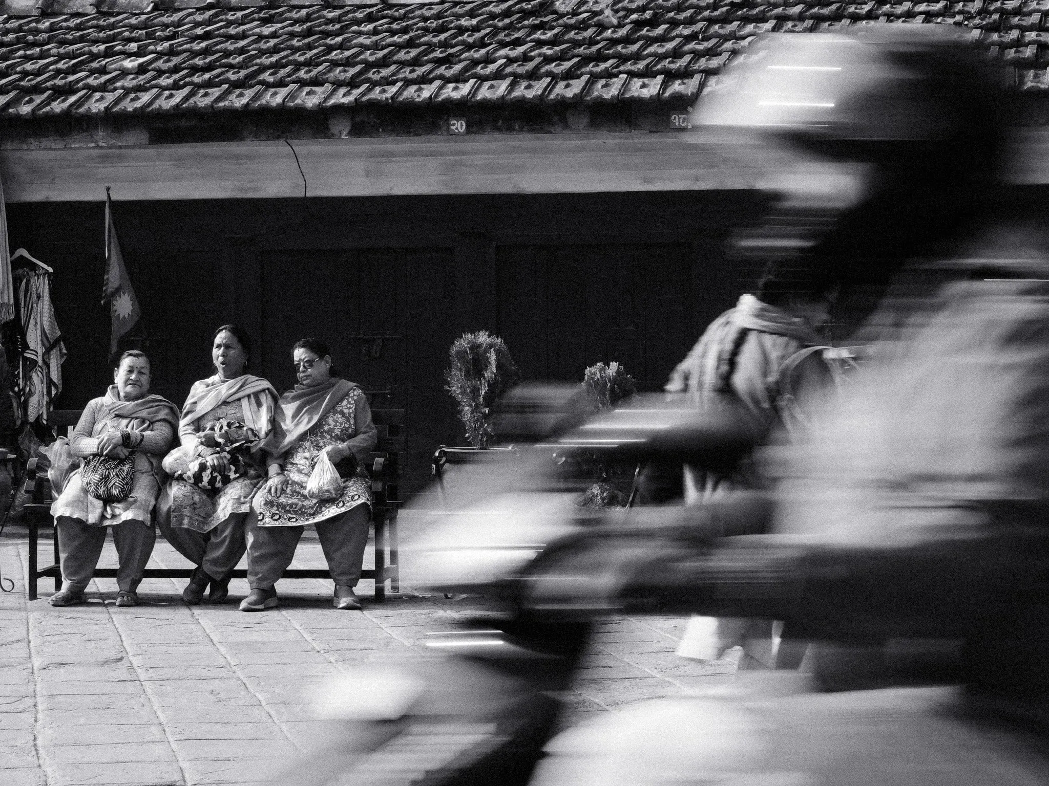 Black and white photo of three women on a bench as a motorbike blurs past