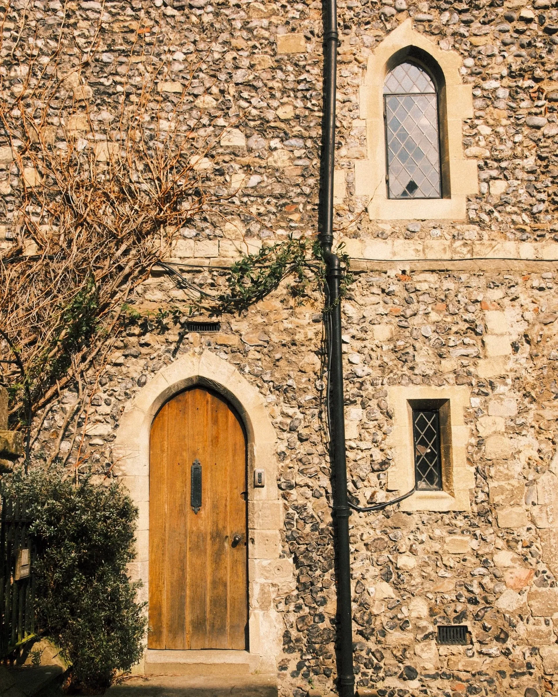 A wooden door and small windows in a flint wall in the cathedral grounds