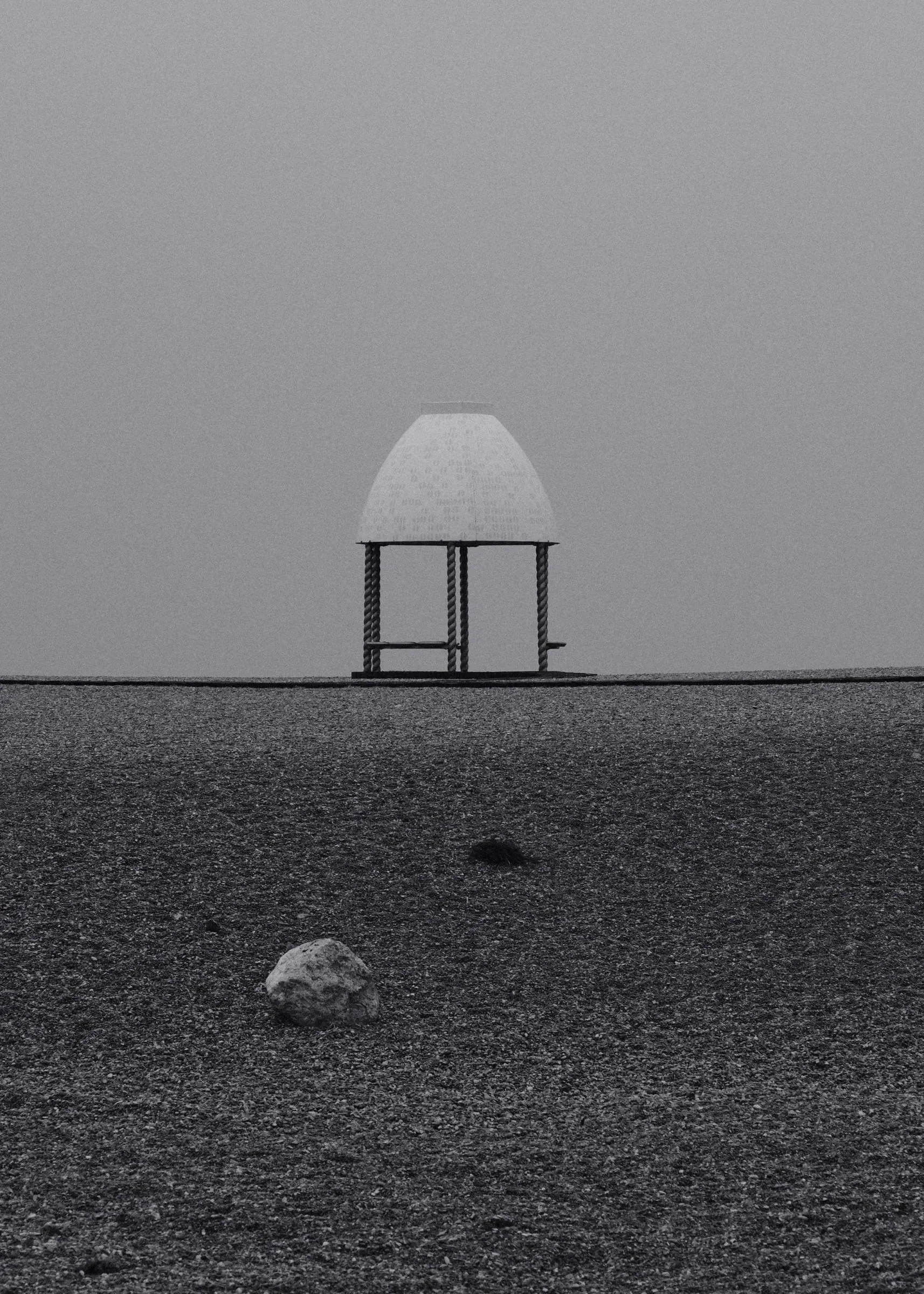 A small domed shelter beyond a stretch of shingle under a grey sky