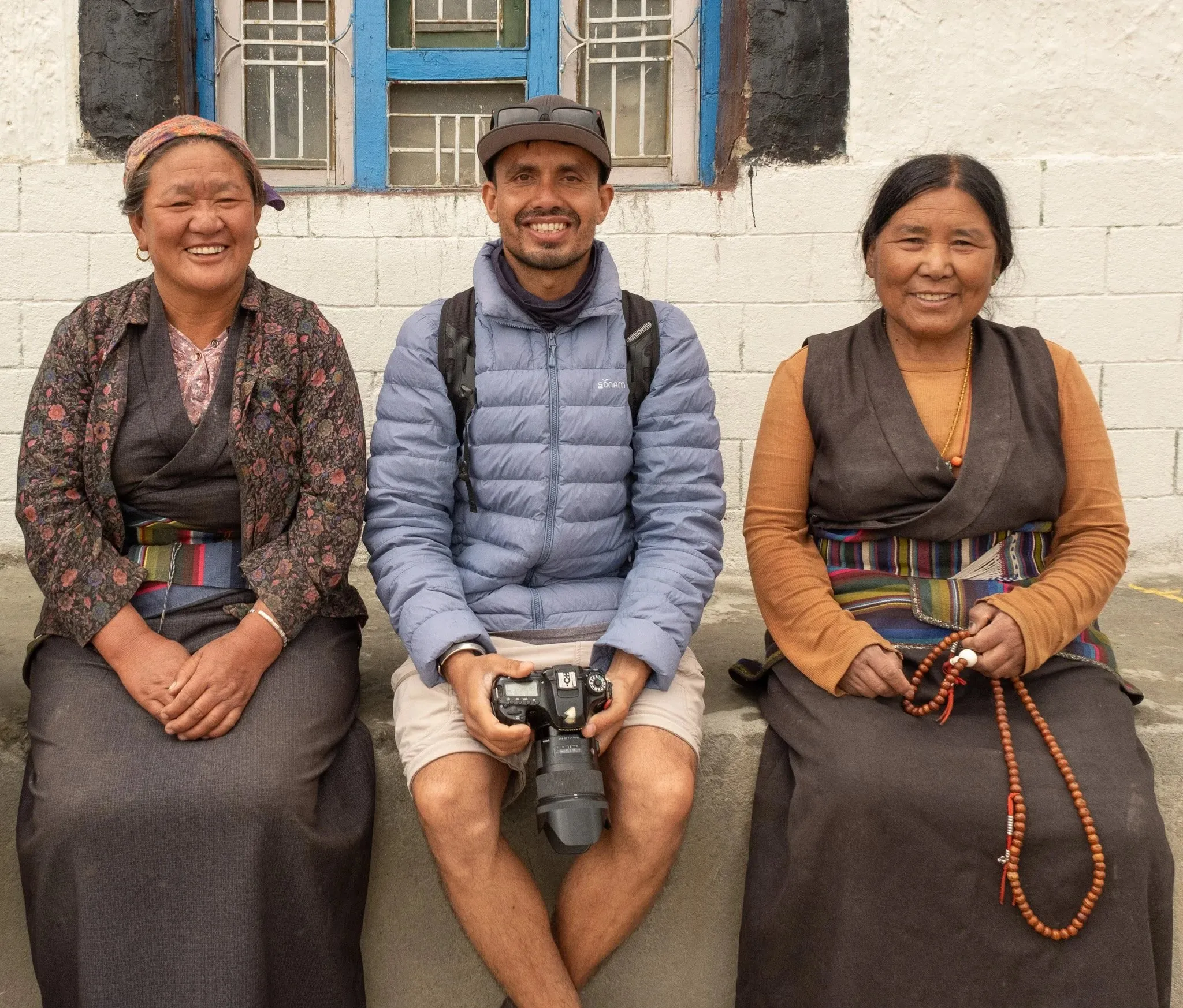 A guide holding a camera, sitting between two smiling women in traditional dress