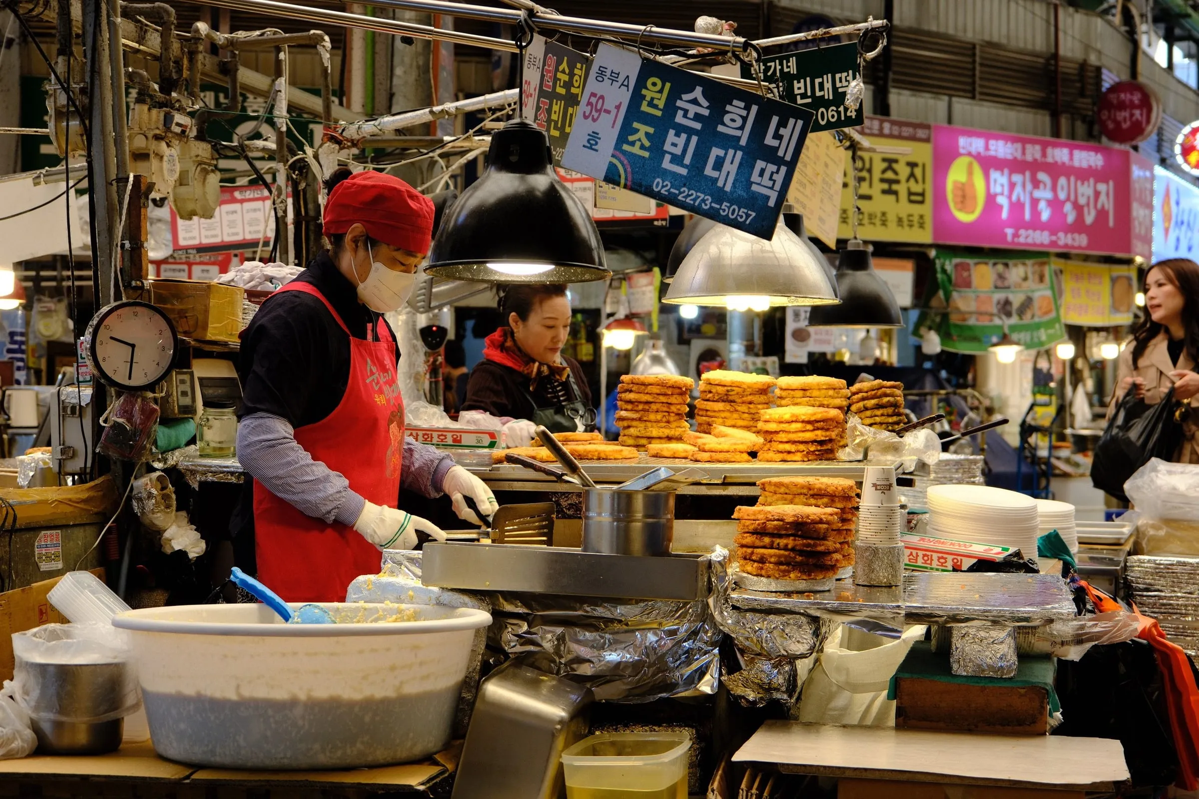 A vendor in a red apron beside stacks of fried pancakes at Gwangjang Market