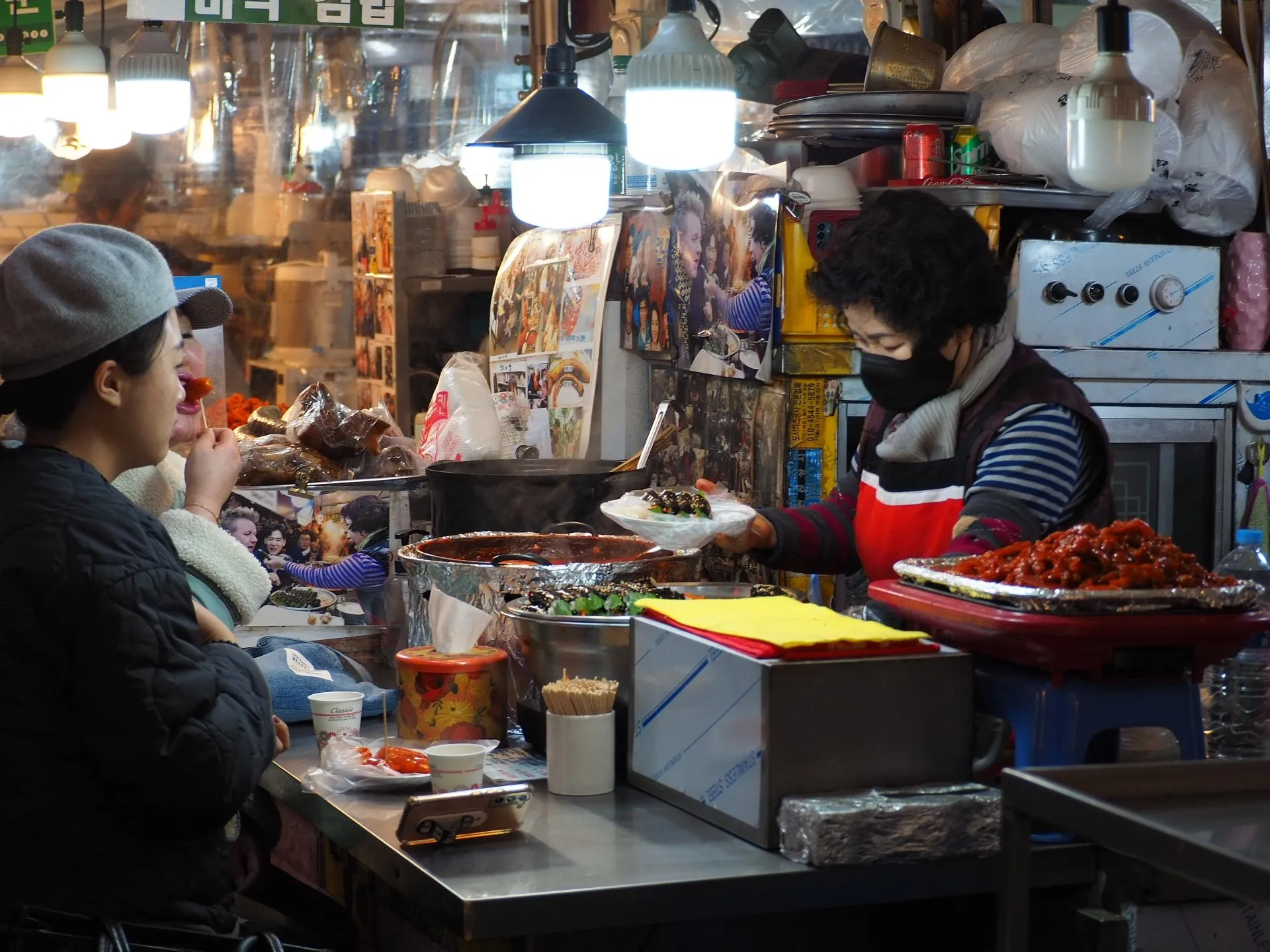 A vendor serves food across a counter to a customer at Gwangjang Market