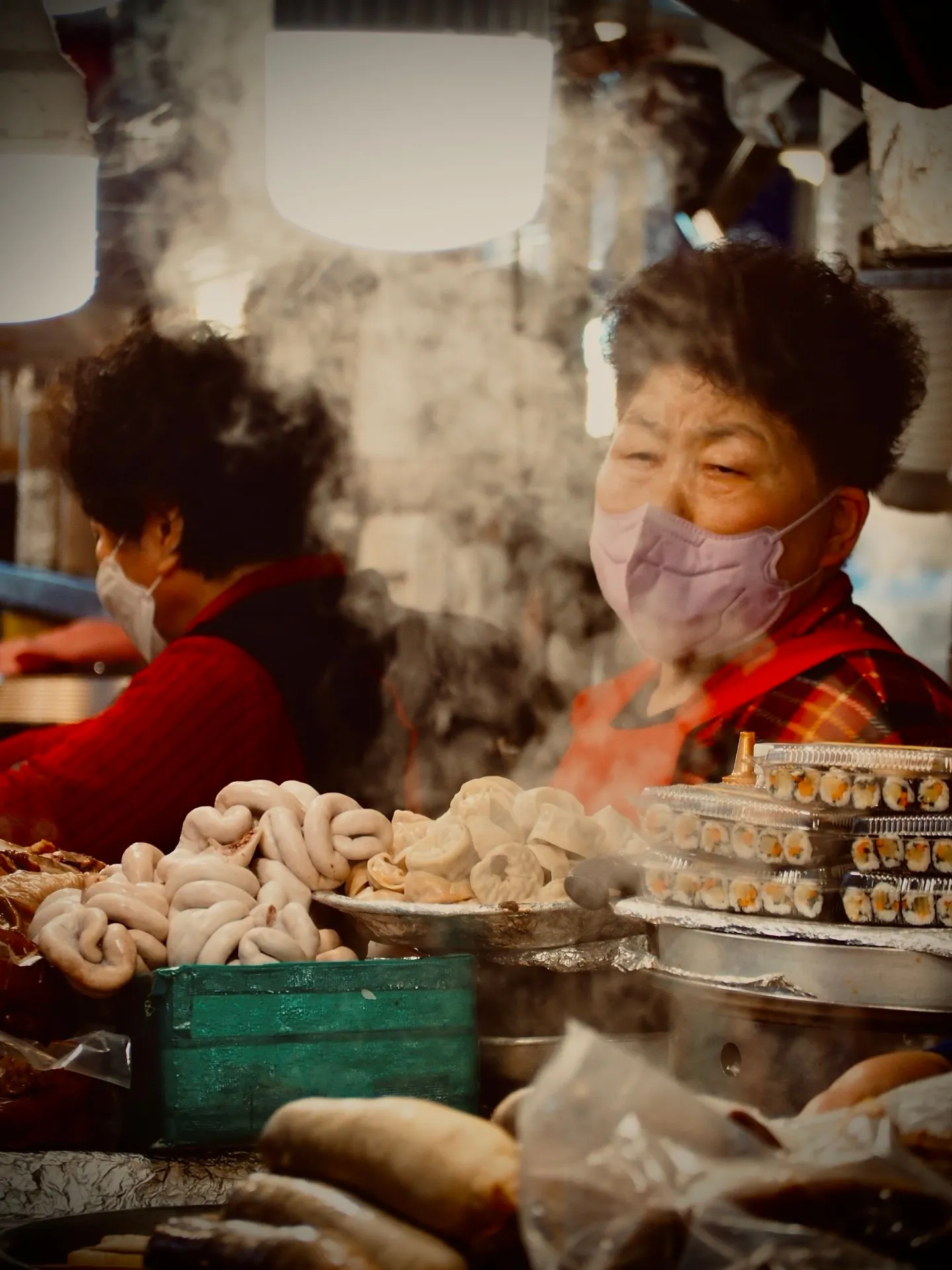 Two vendors behind rising steam and trays of sundae and kimbap at Gwangjang Market