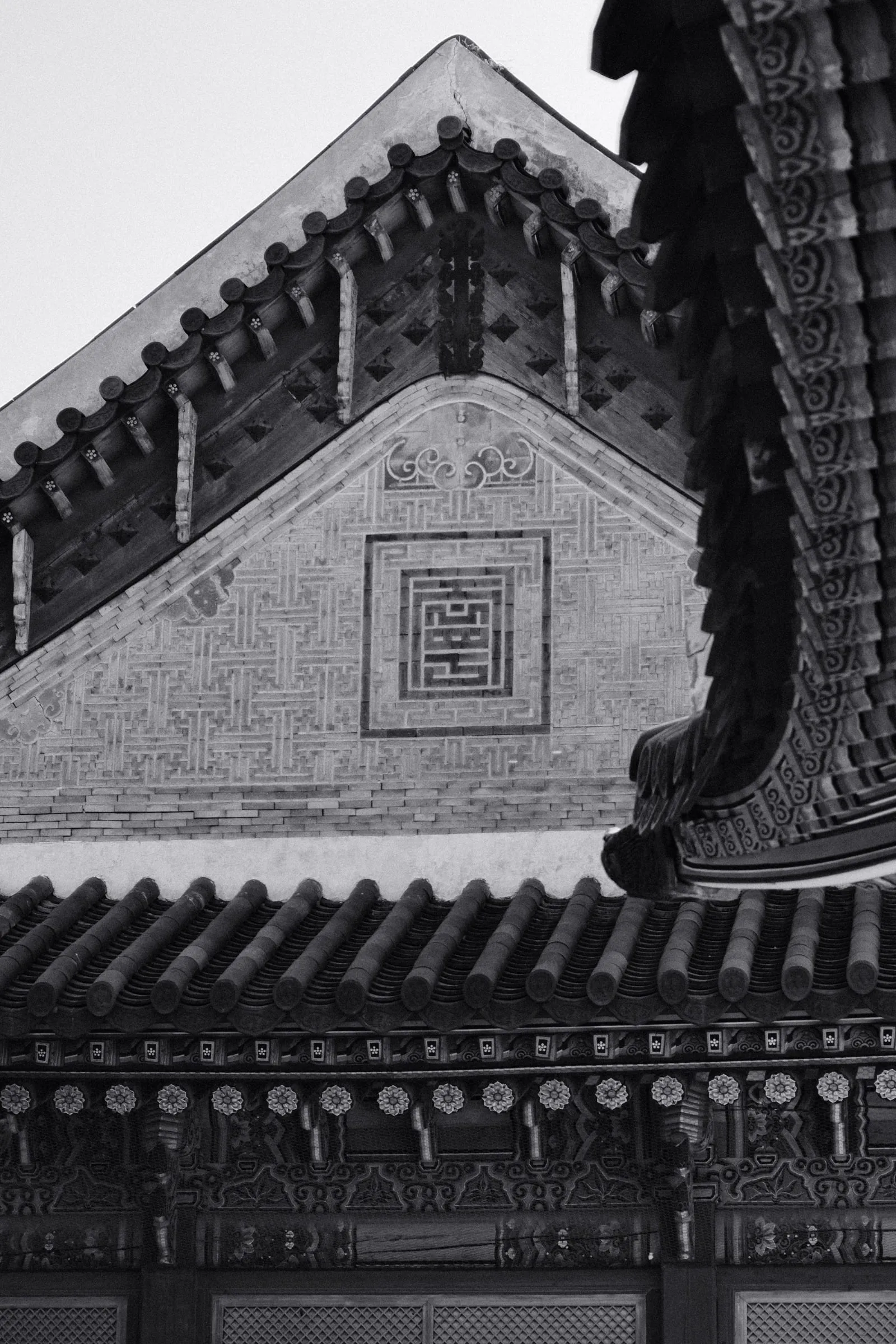 Black and white detail of a patterned gable and tiled roofs at Gyeongbokgung Palace