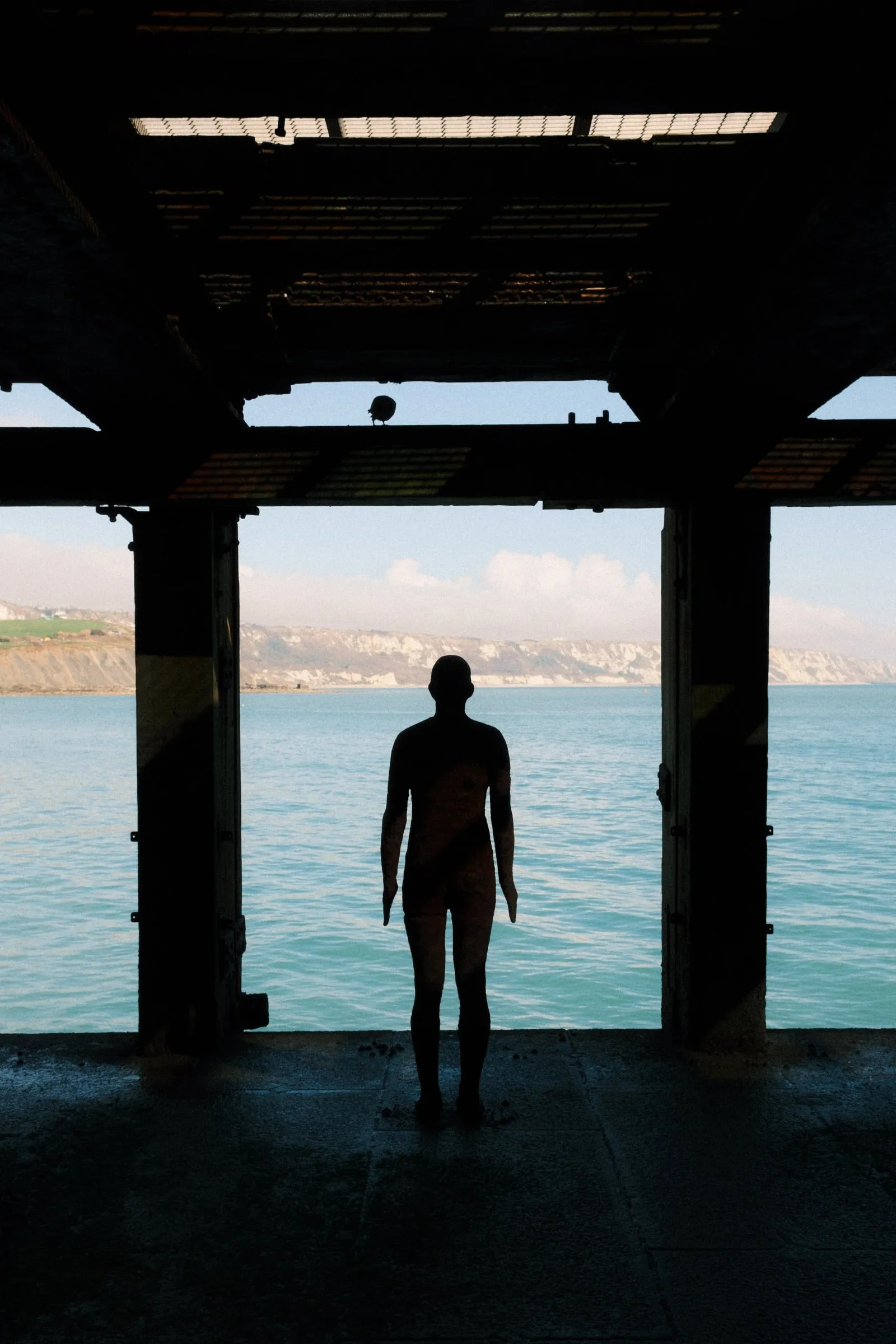A statue in silhouette beneath the Harbour Arm, looking out to sea