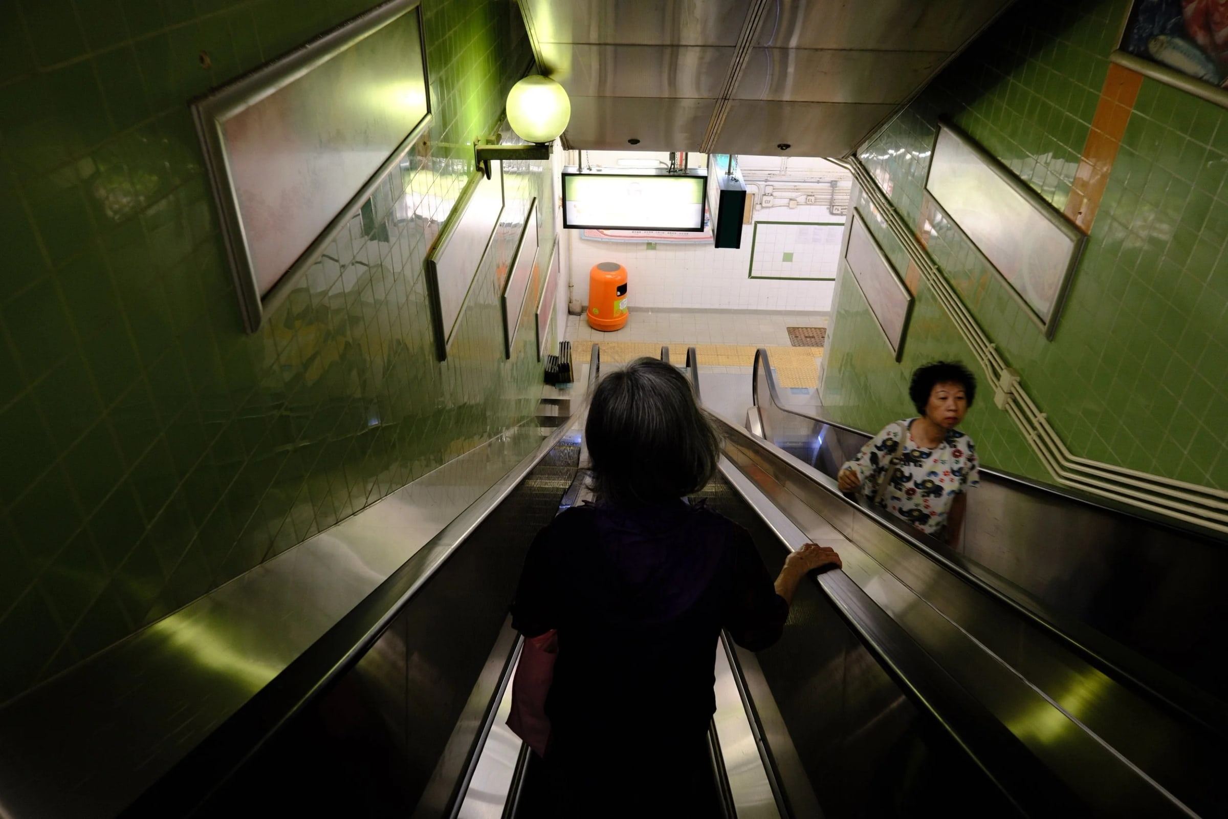 People riding a long escalator through a green-tiled tunnel