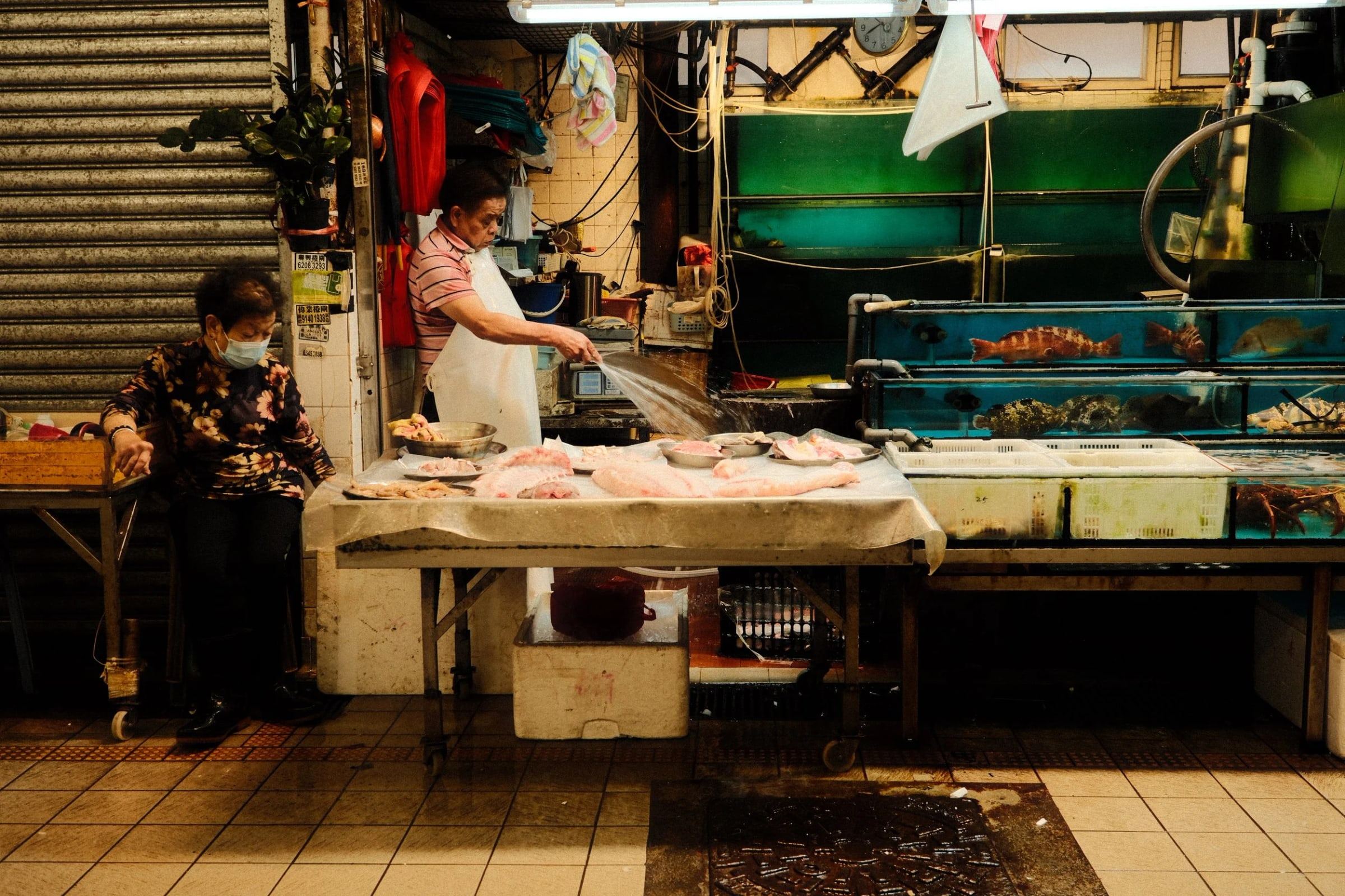 Fishmonger preparing fish at a market stall beside aquarium tanks