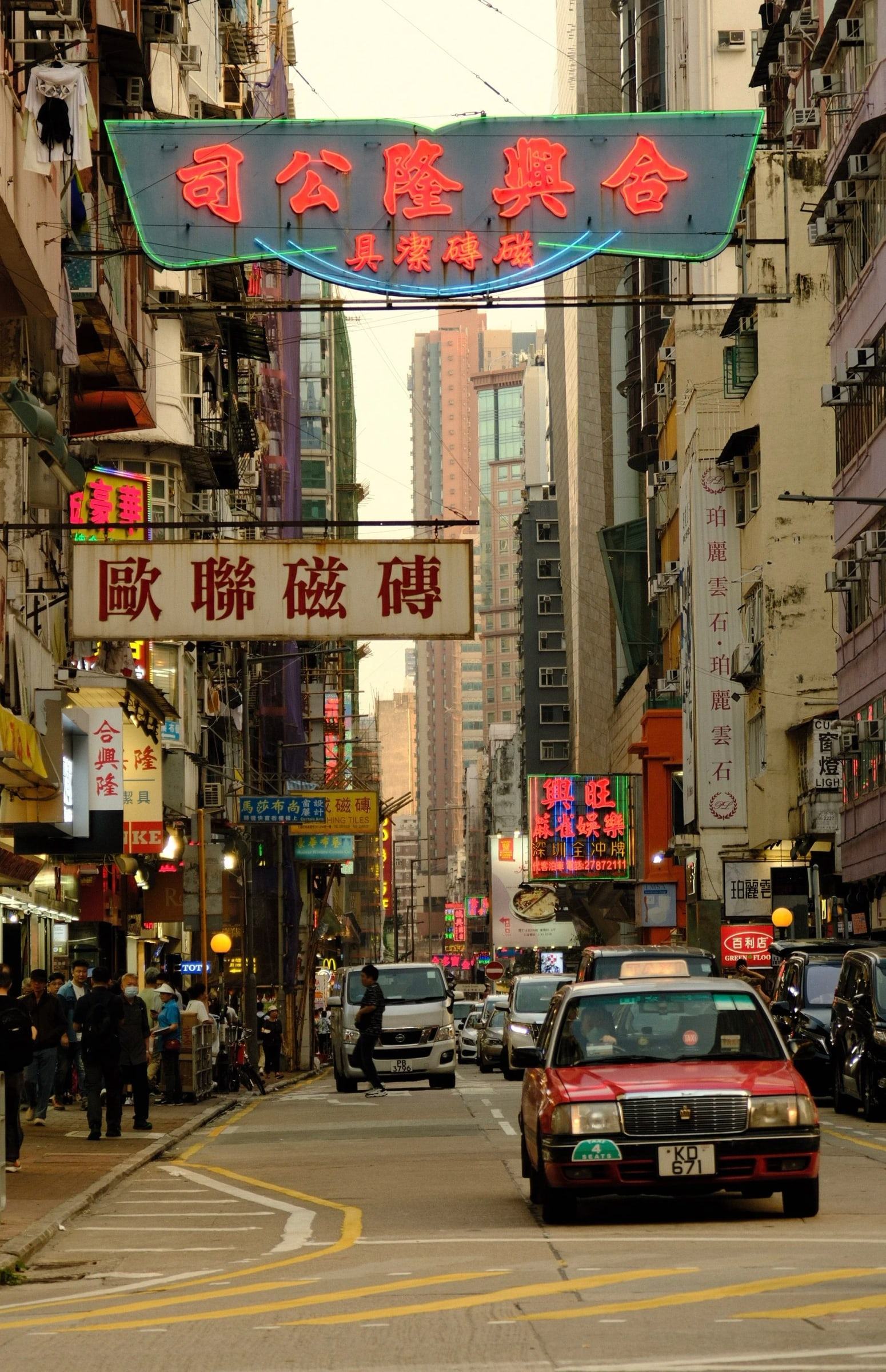 Red taxi driving down a street lined with hanging signs