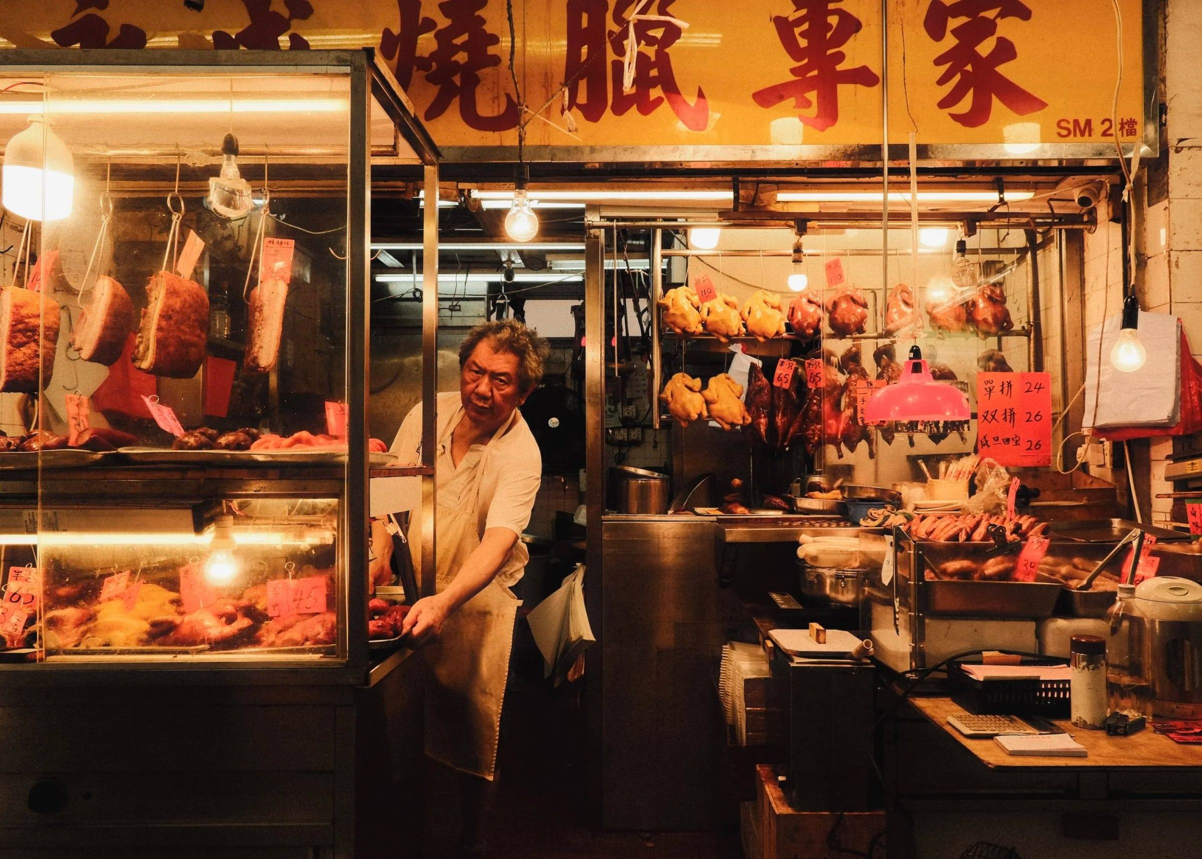 Man working in a roast meat shop beneath a red and gold sign