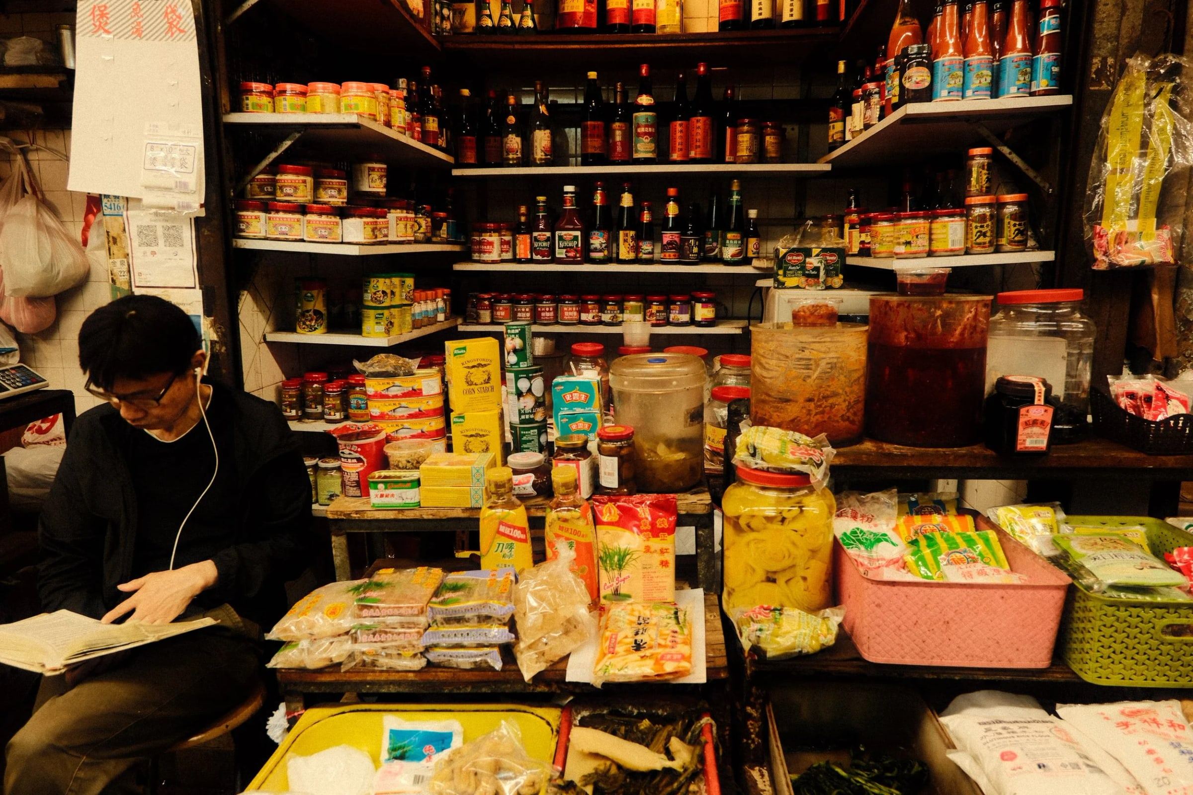 Shopkeeper reading among shelves packed with bottles and snacks