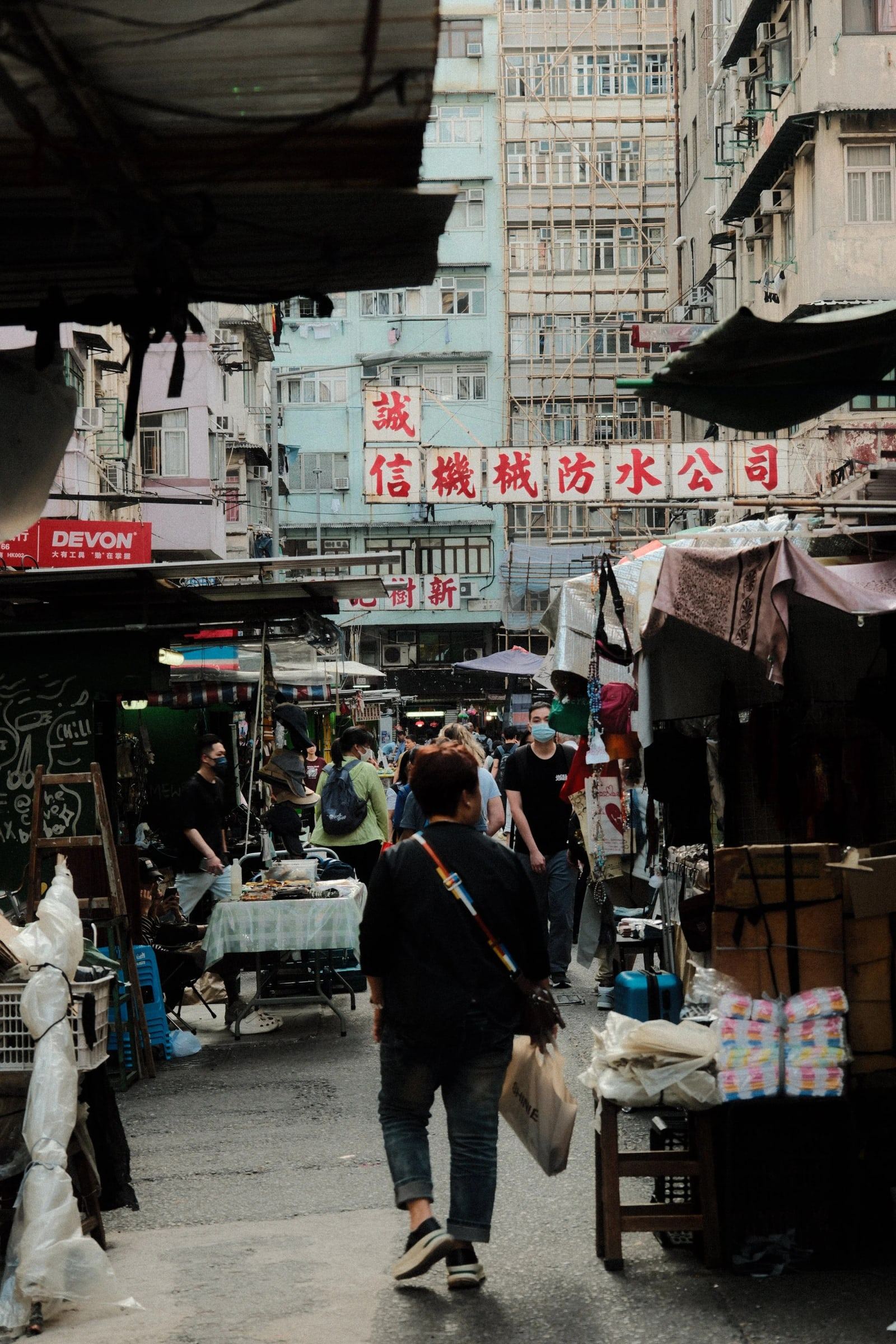 Man carrying shopping bags past street market stalls and old apartment blocks